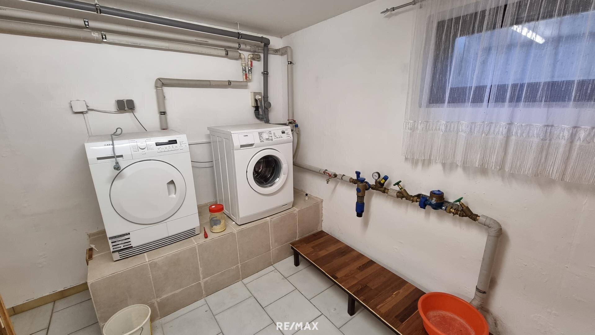 Waschküche im Keller mit Waschmaschine, Trockner und Versorgungsleitungen.