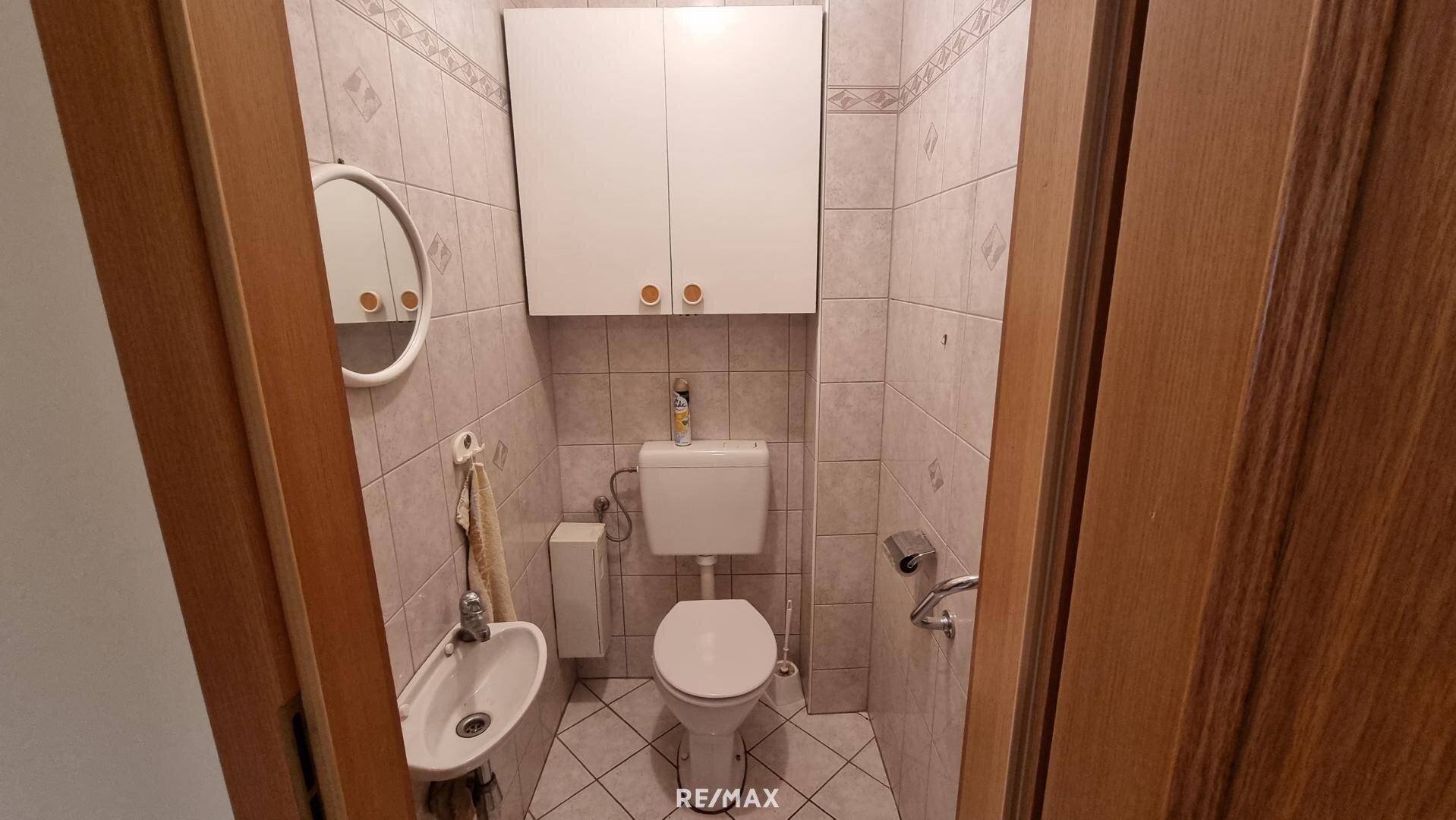 Separate Gästetoilette mit WC, kleinem Waschbecken und Wandfliesen.
