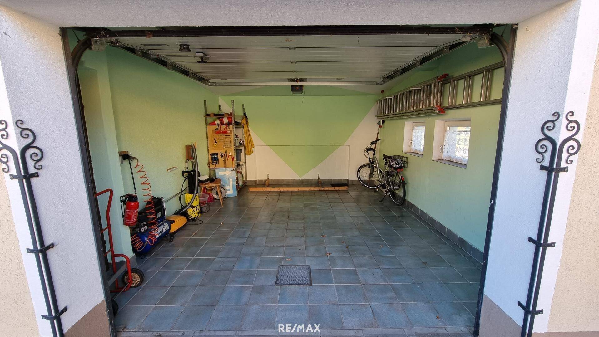 Geräumige Garage mit Fliesenboden und Platz für Fahrzeuge und Fahrräder.