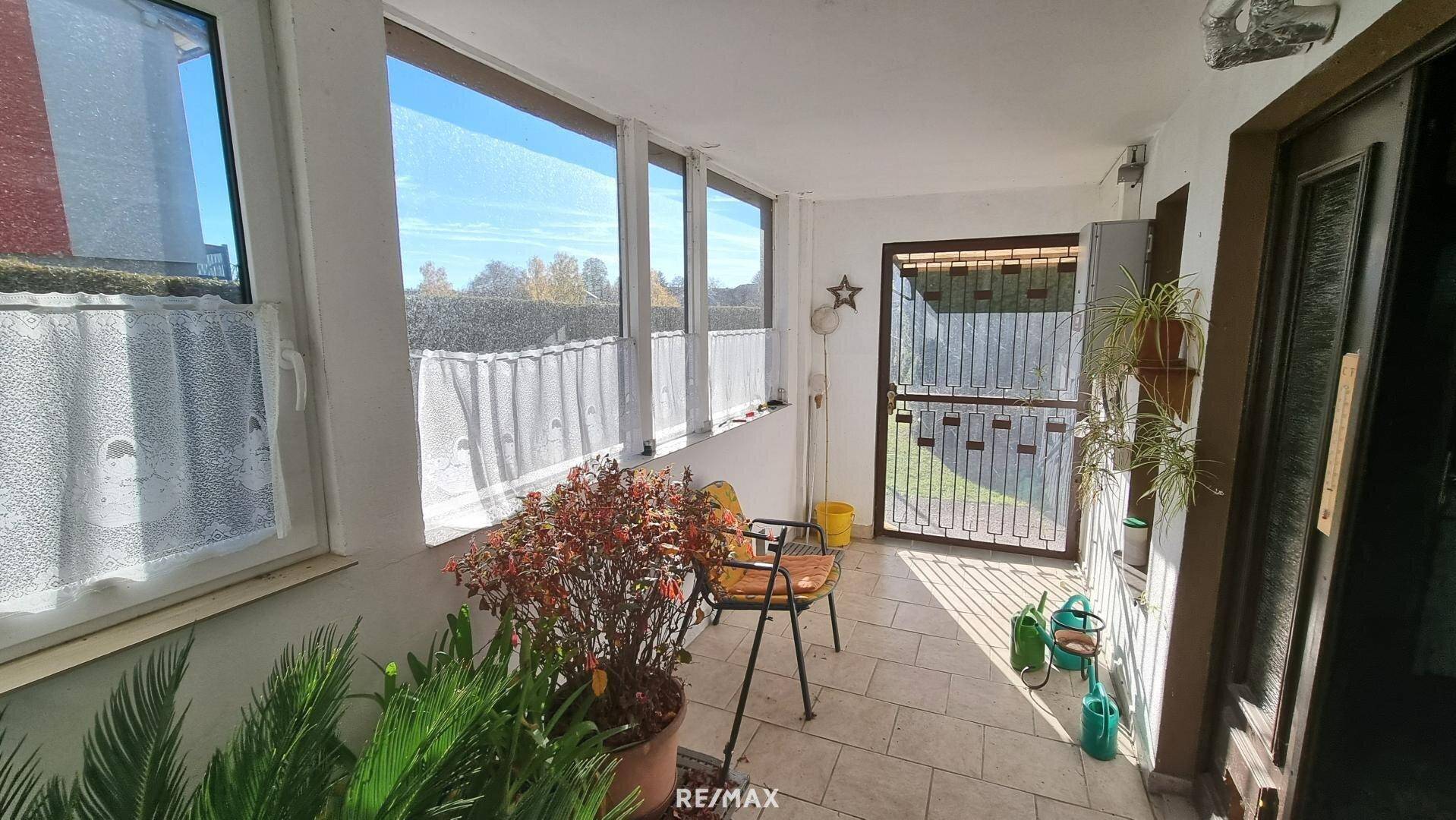 Überdachte Loggia mit Fliesenboden, vielen Fenstern und Blick in den Garten.