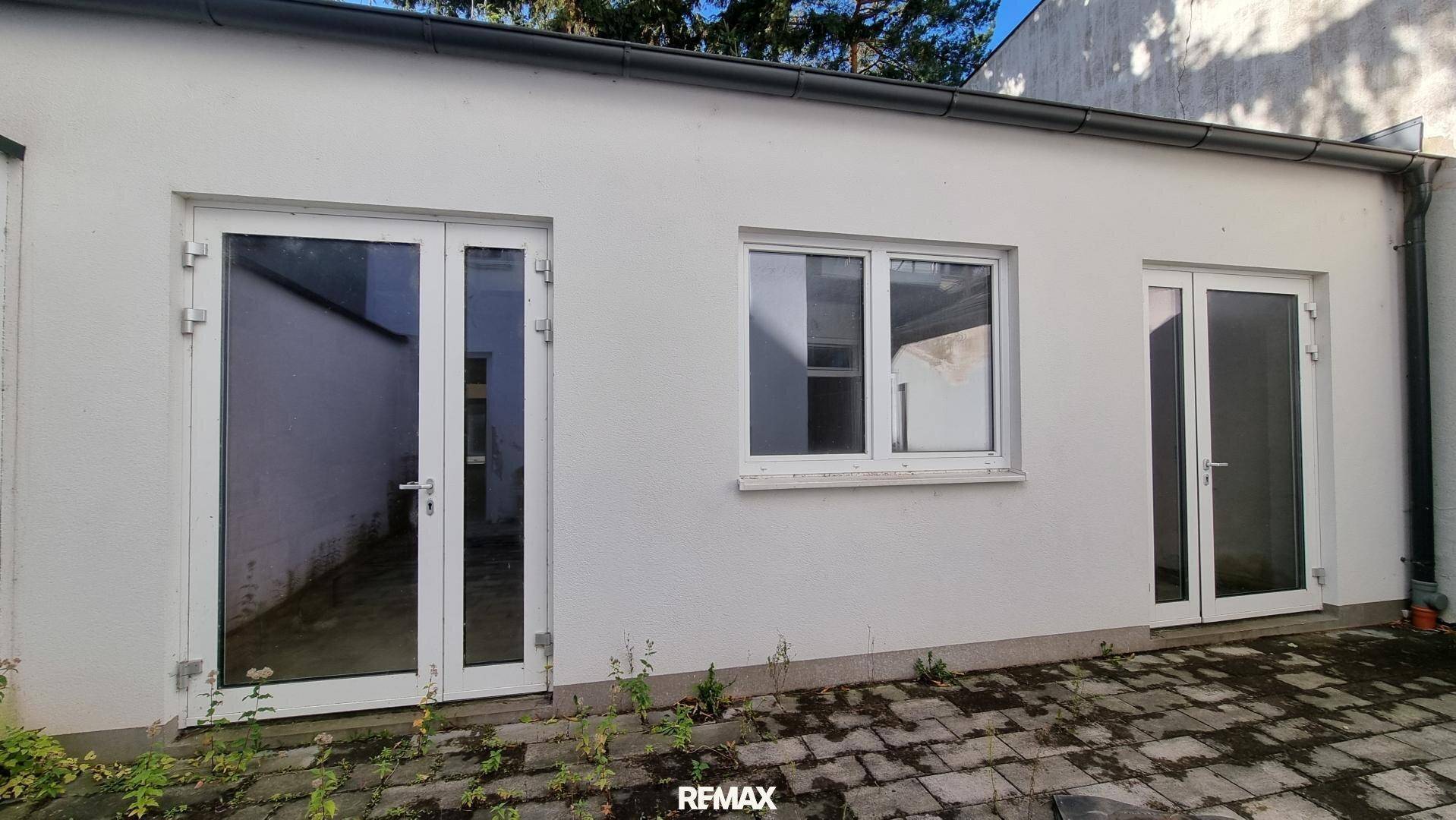 Rückseite eines Gebäudes mit zwei Glastüren und einem Fenster, die zu einem gepflasterten Bereich führen.