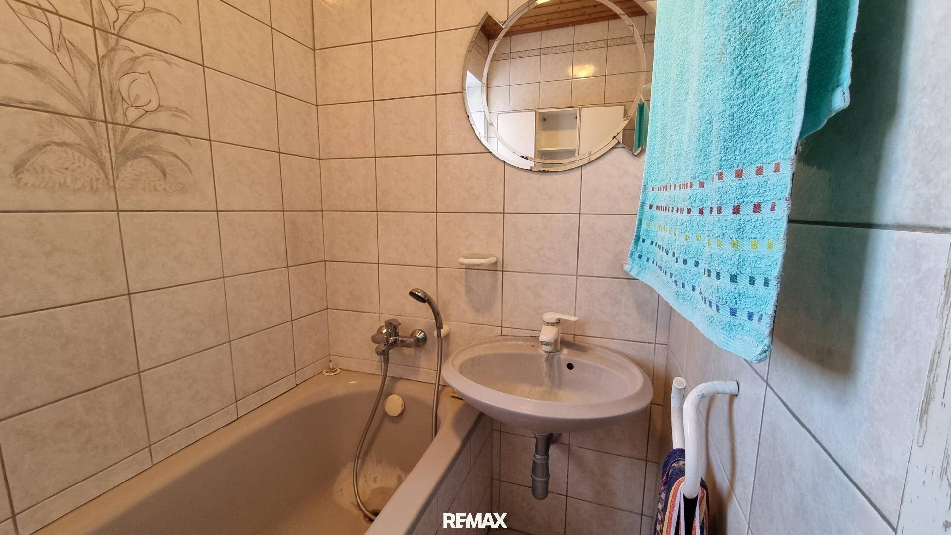 Kleines Badezimmer mit Badewanne, Waschbecken und Fliesen, in einfachem Zustand.