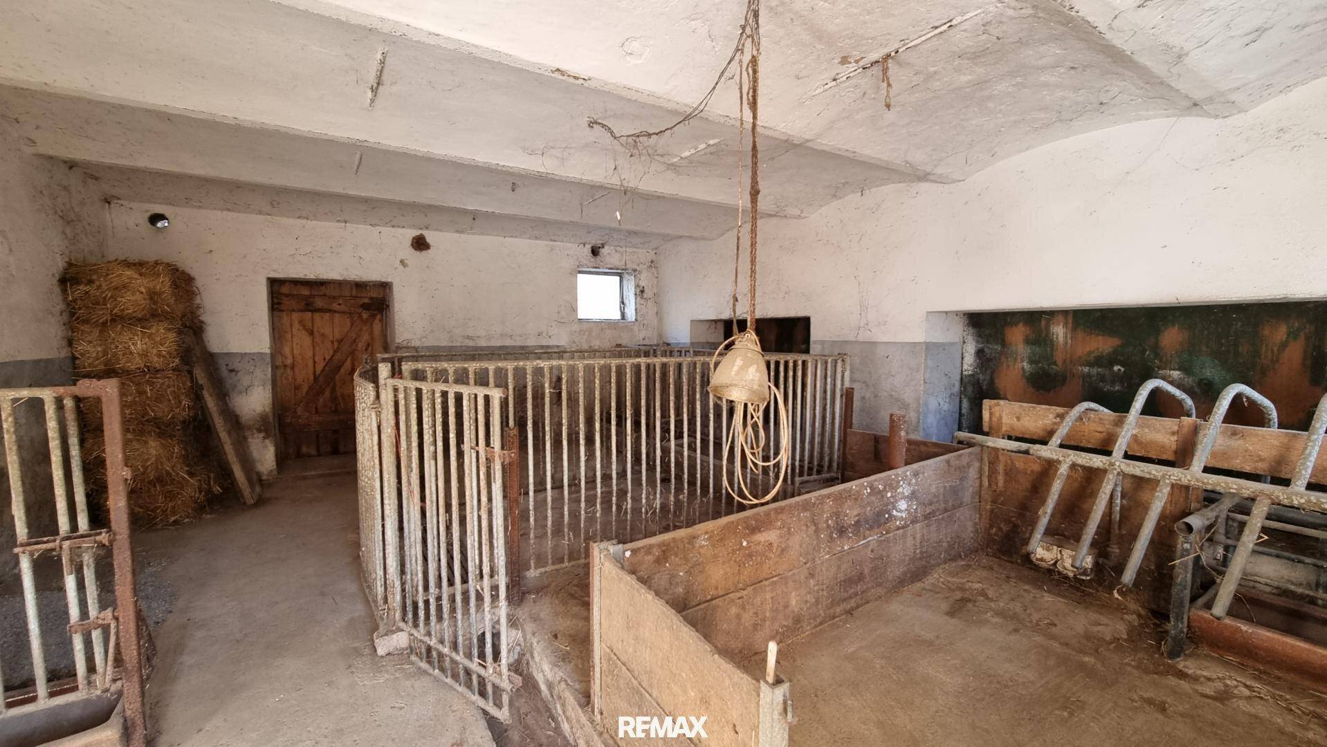 Innenansicht eines Stalls mit Tierboxen, Heuballen und landwirtschaftlichen Geräten.