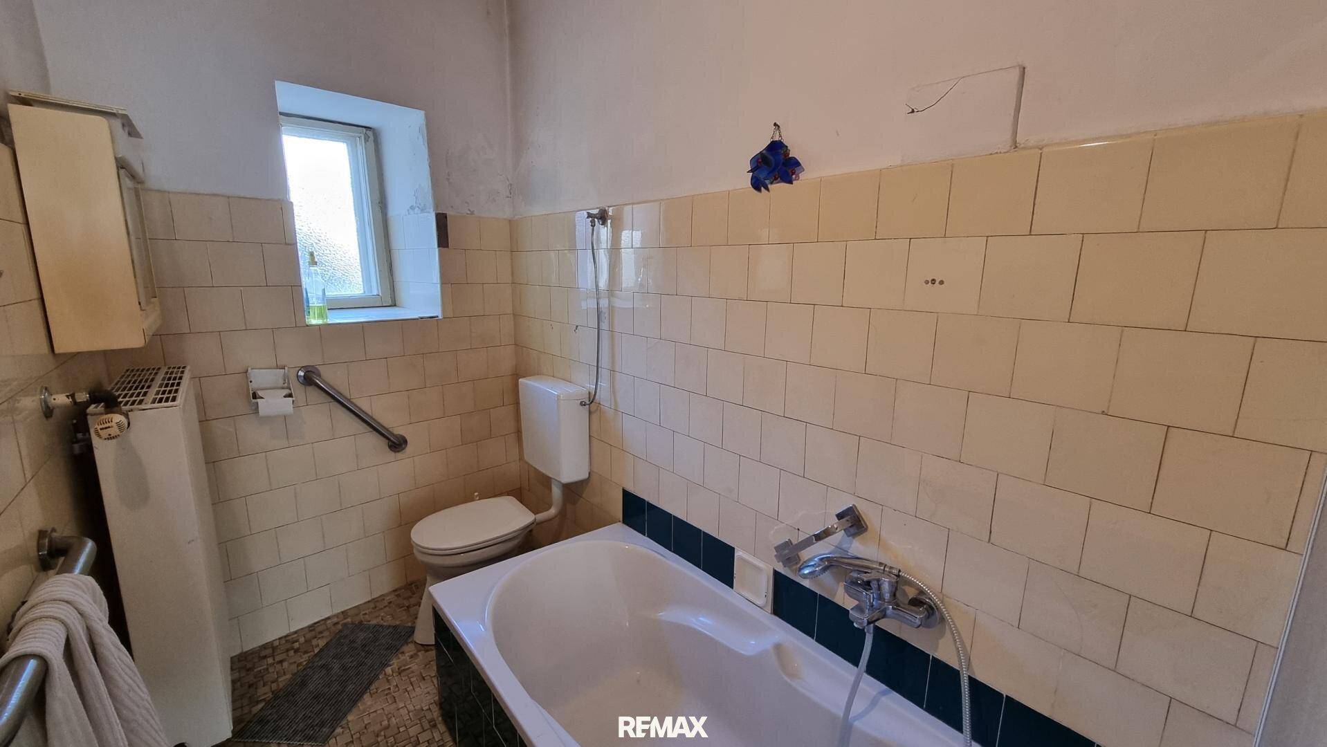 Badezimmer mit beigefarbenen Fliesen, Badewanne, Toilette und einem kleinen Fenster.