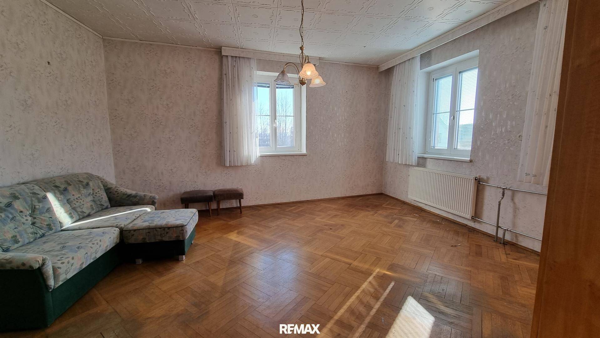 Wohnzimmer mit Fischgrätparkett, Sofa und zwei Fenstern, die den Raum erhellen.