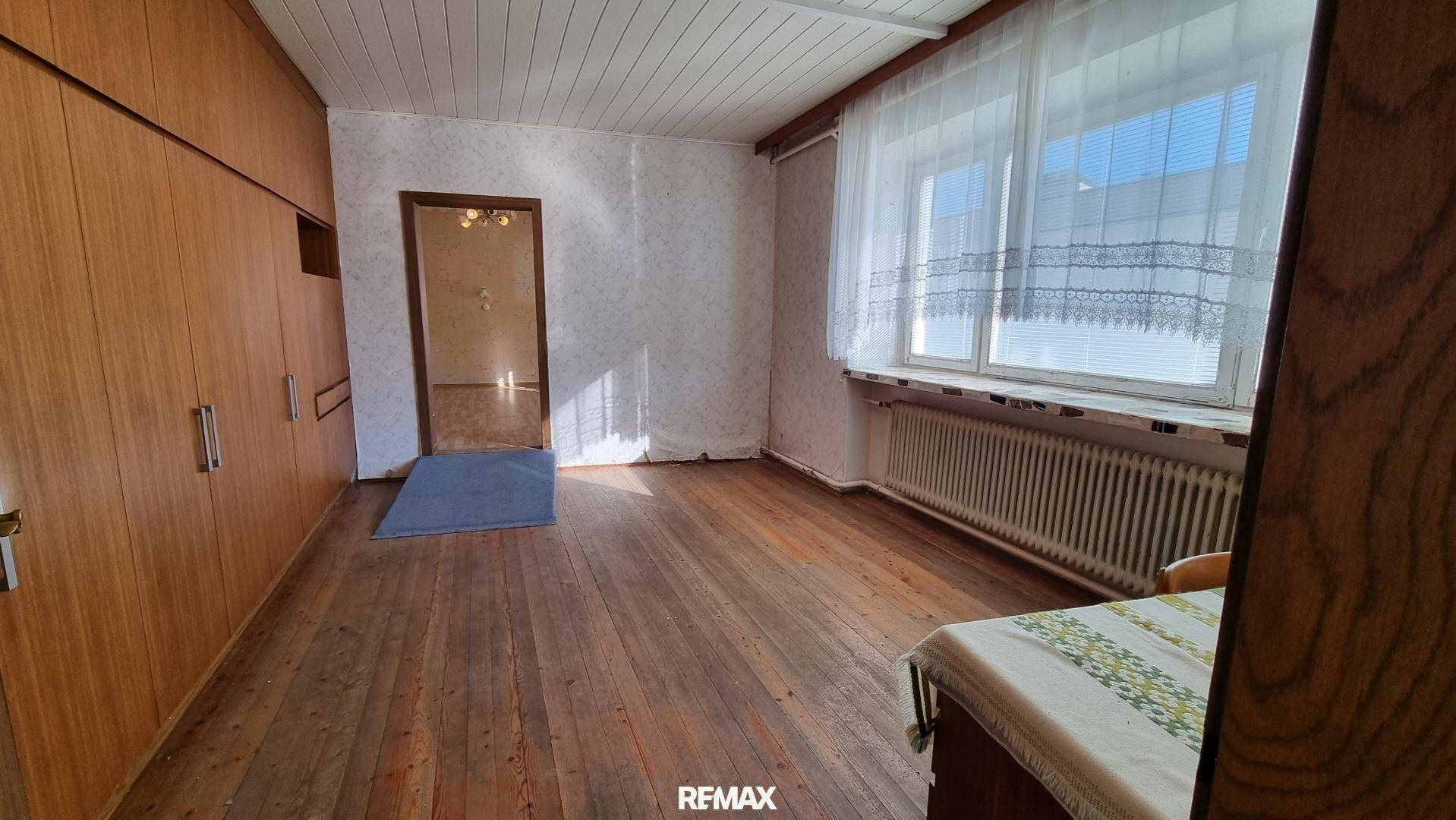 Schlafzimmer mit Holzdielenboden, Einbauschränken und einem großen Fenster mit viel Tageslicht.