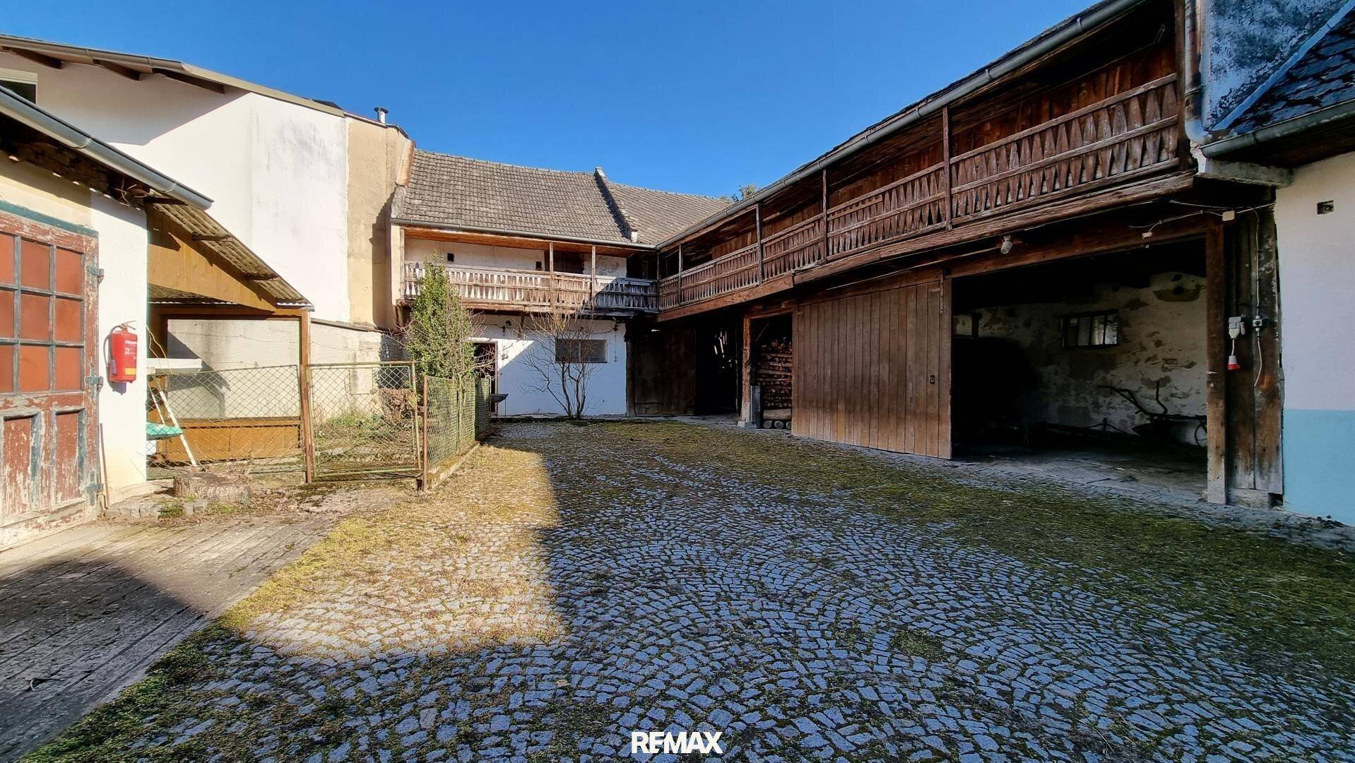 Weitläufiger gepflasterter Hof, umgeben von historischen Gebäuden mit Holzbalkonen und Scheunentoren.