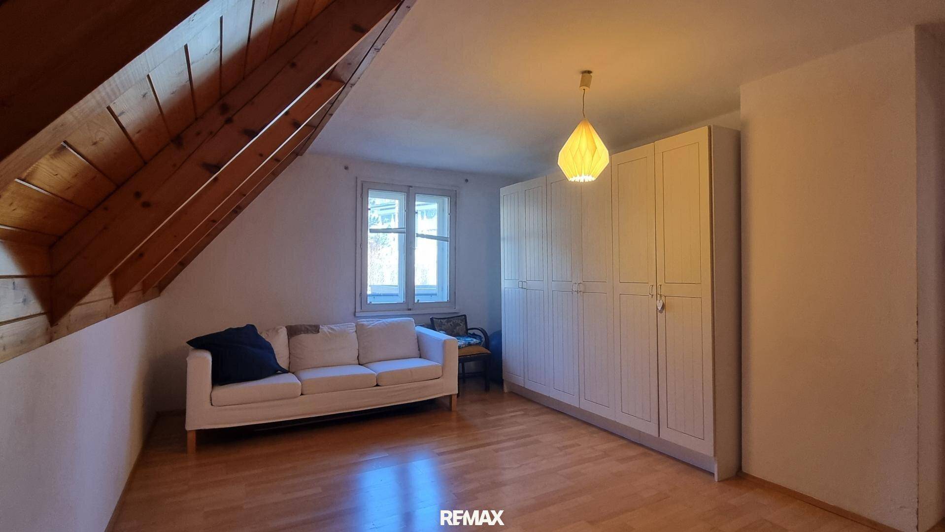 Geräumiges Dachzimmer mit Holzboden, Dachschräge und weißem Sofa.