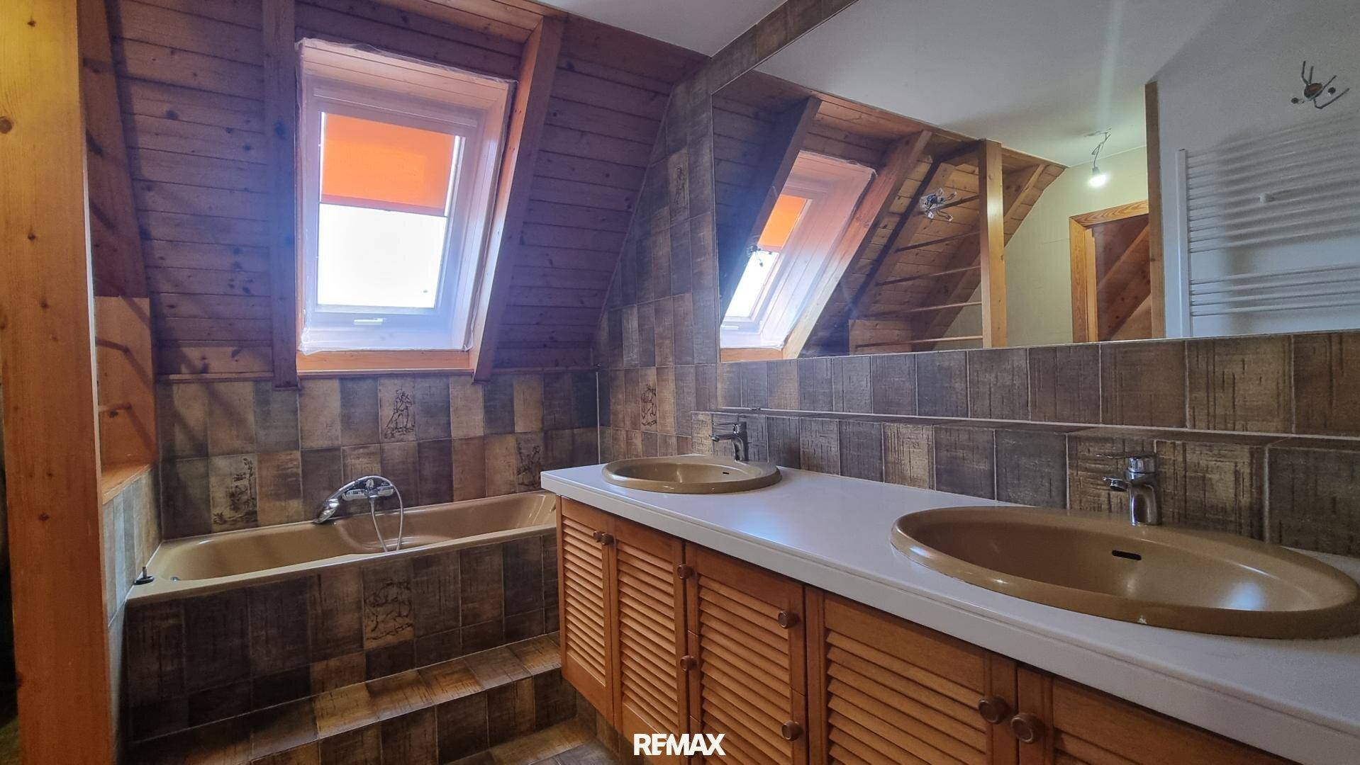 Badezimmer im Dachgeschoss mit Holzverkleidung, Badewanne und Doppelwaschbecken unter Dachfenstern.