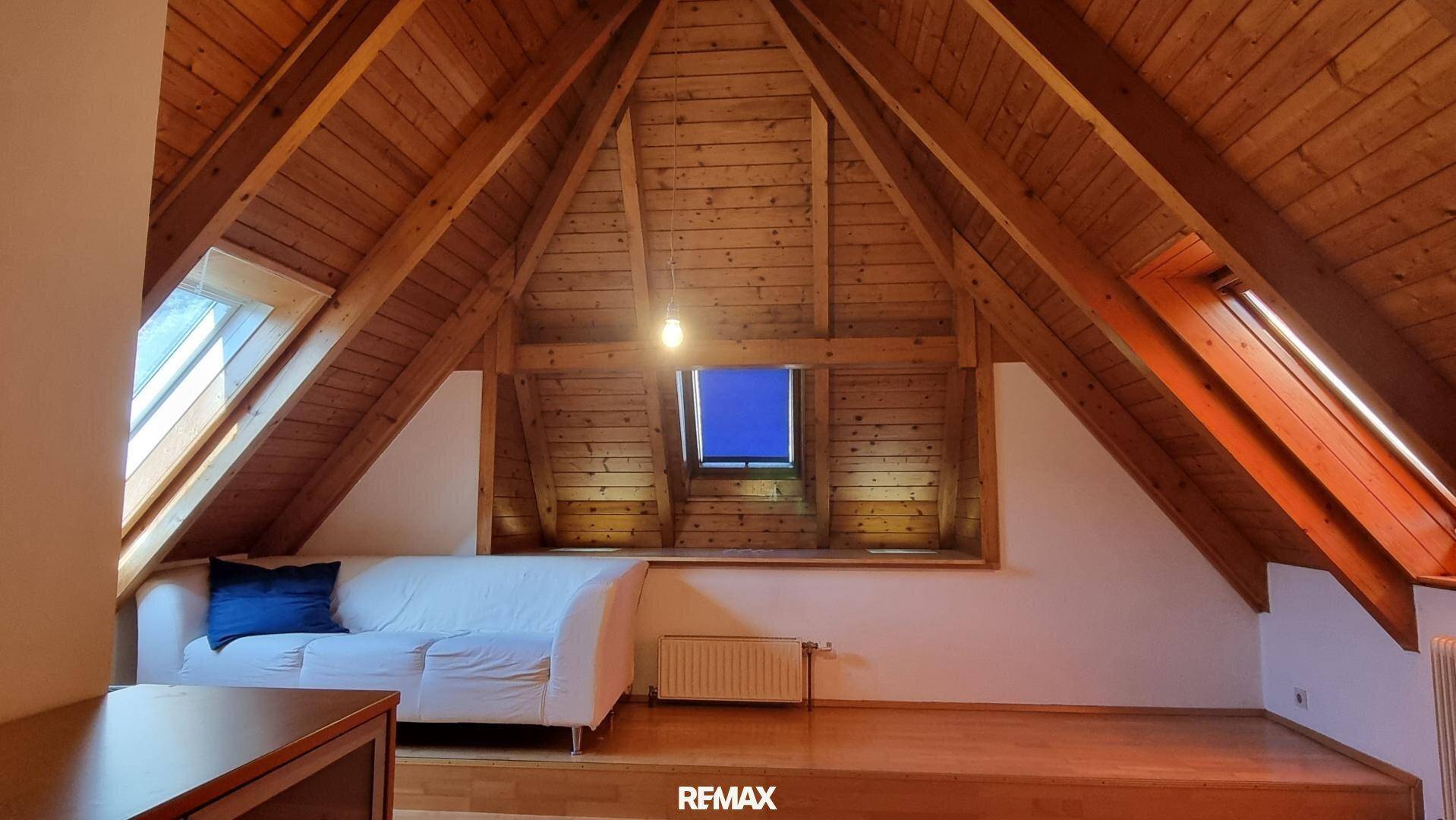 Gemütlicher Wohnbereich im Dachgeschoss mit Sofa, Holzbalken und Dachfenstern.