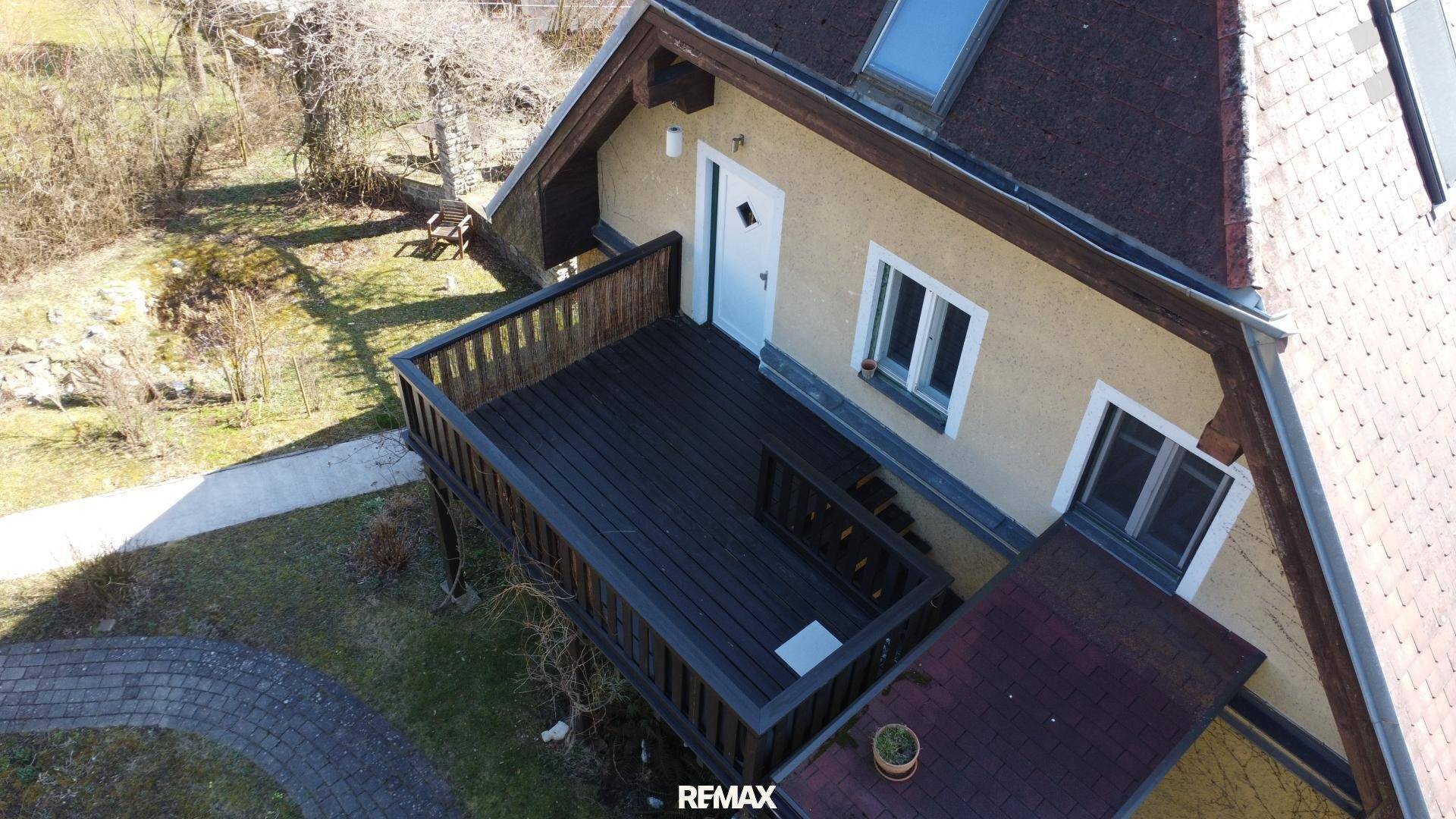 Großer Holzbalkon mit Geländer und Zugang zum Haus, umgeben von Natur.
