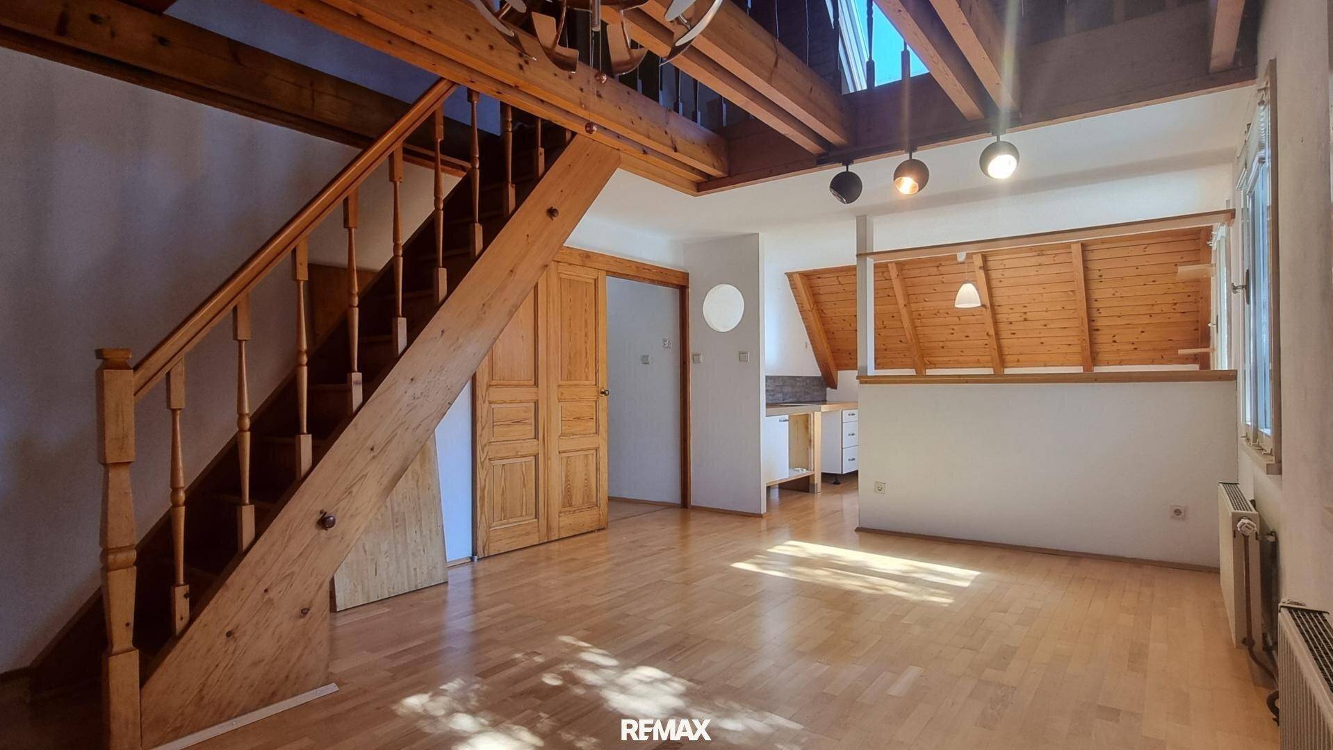 Offener Wohnbereich im Dachgeschoss mit Holzbalken, Treppe und Holzboden.