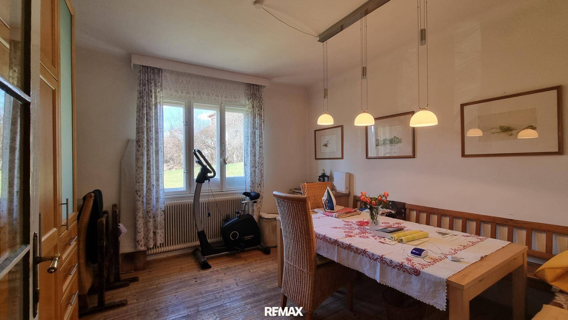 Esszimmer mit Holztisch, Bank und Heimtrainer, hell durch große Fenster.
