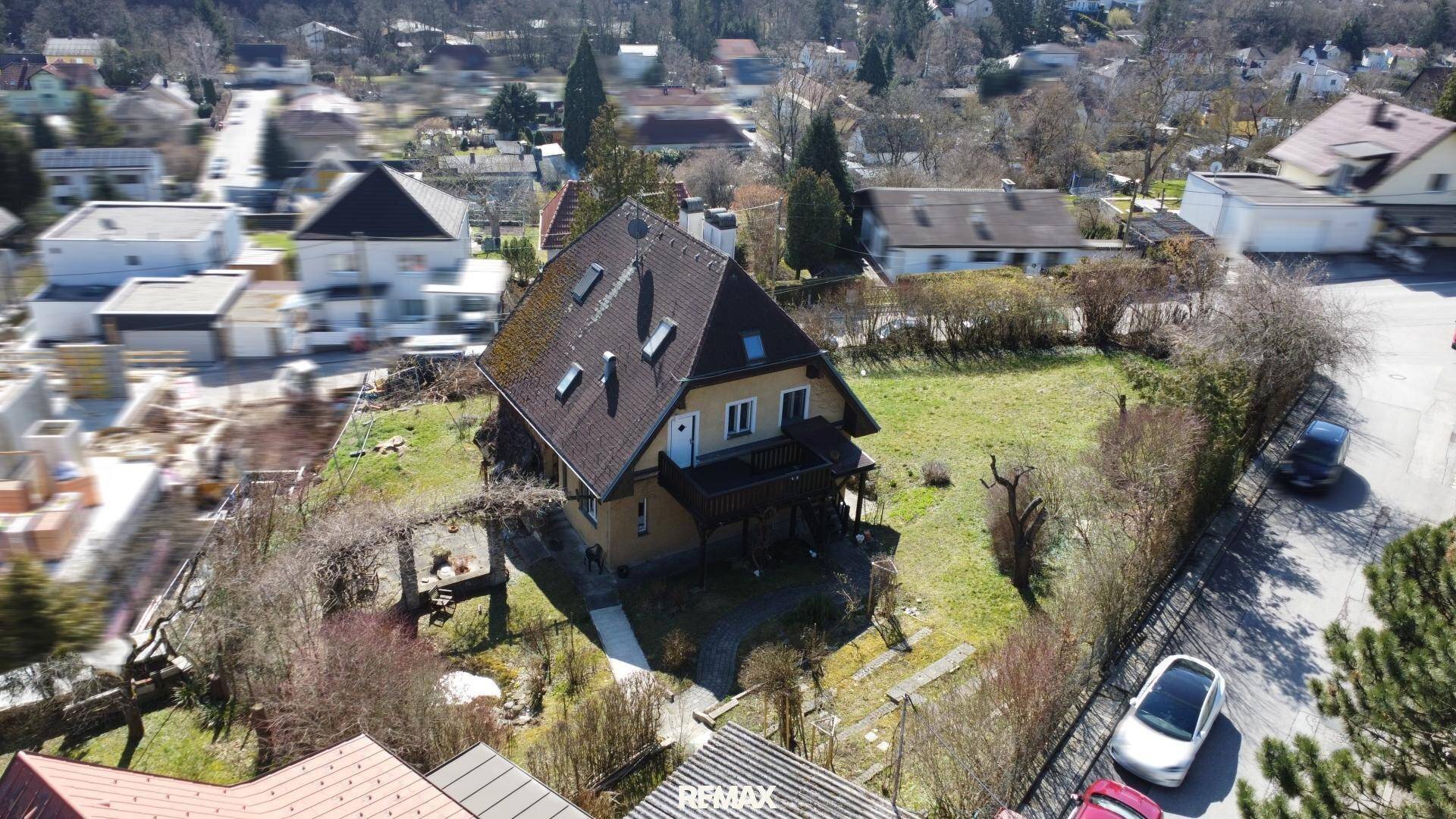Vogelperspektive eines Einfamilienhauses mit Garten und umliegender Bebauung unter blauem Himmel.