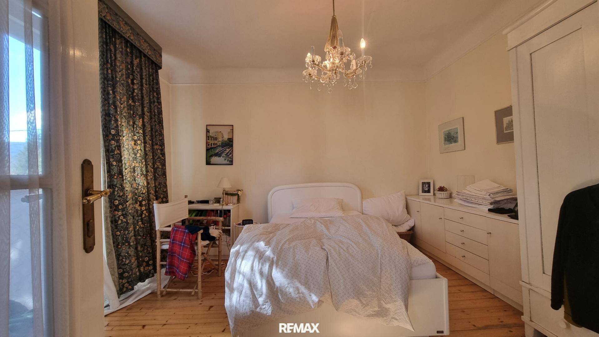 Helles Schlafzimmer mit Holzboden, weißem Bett und Kronleuchter, mit Zugang zum Balkon.