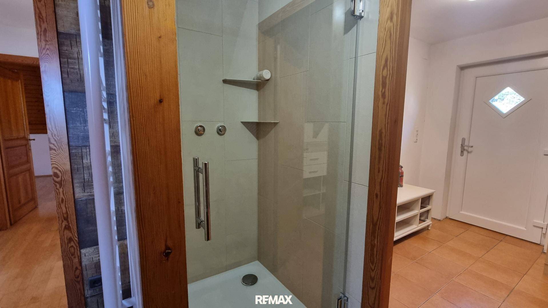 Modernisierte Dusche mit Glasabtrennung und Fliesen, umgeben von Holzdetails.