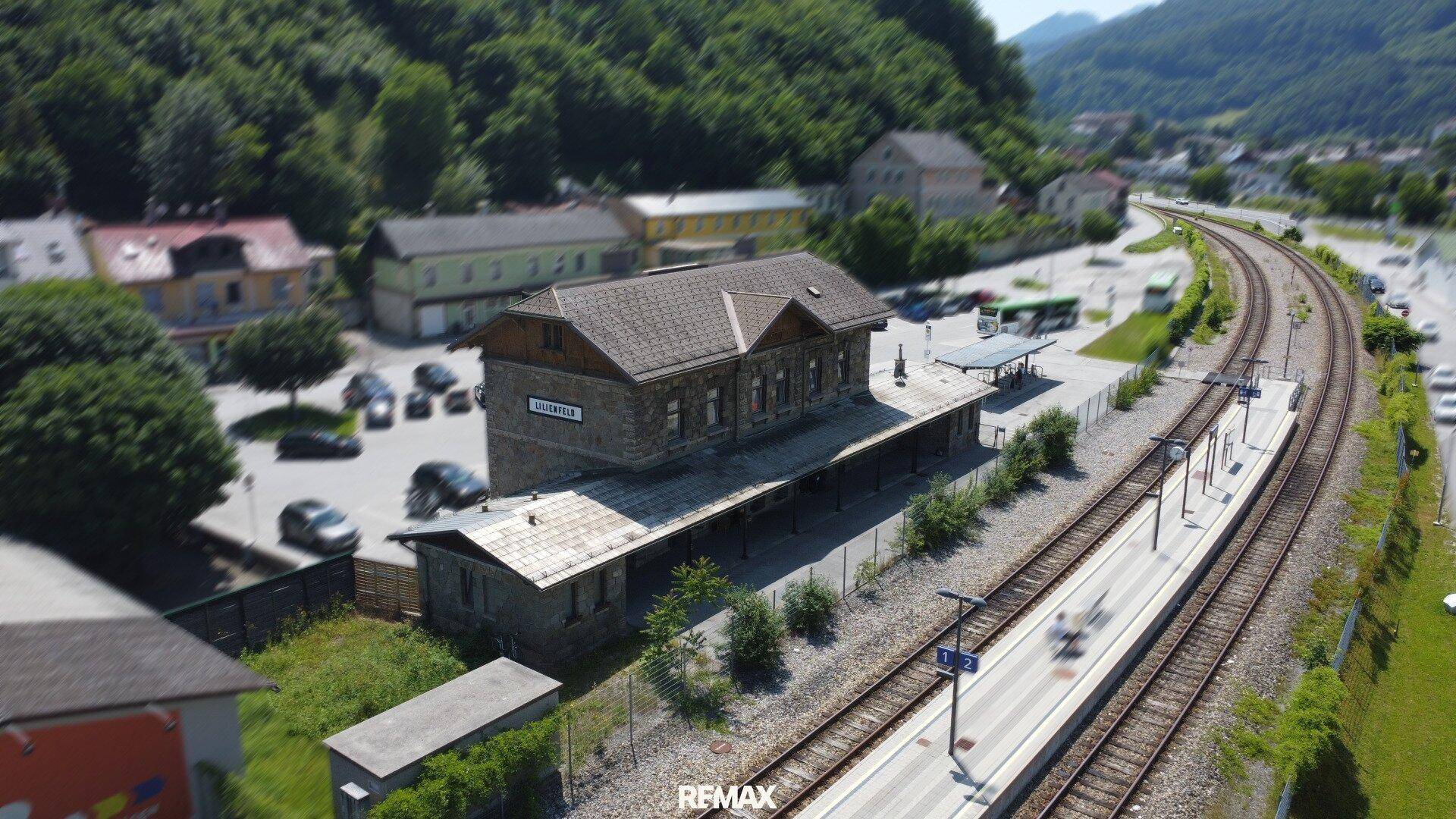 Weitläufige Luftaufnahme des Bahnhofs Lilienfeld mit geschwungenen Bahngleisen und der umliegenden Landschaft.