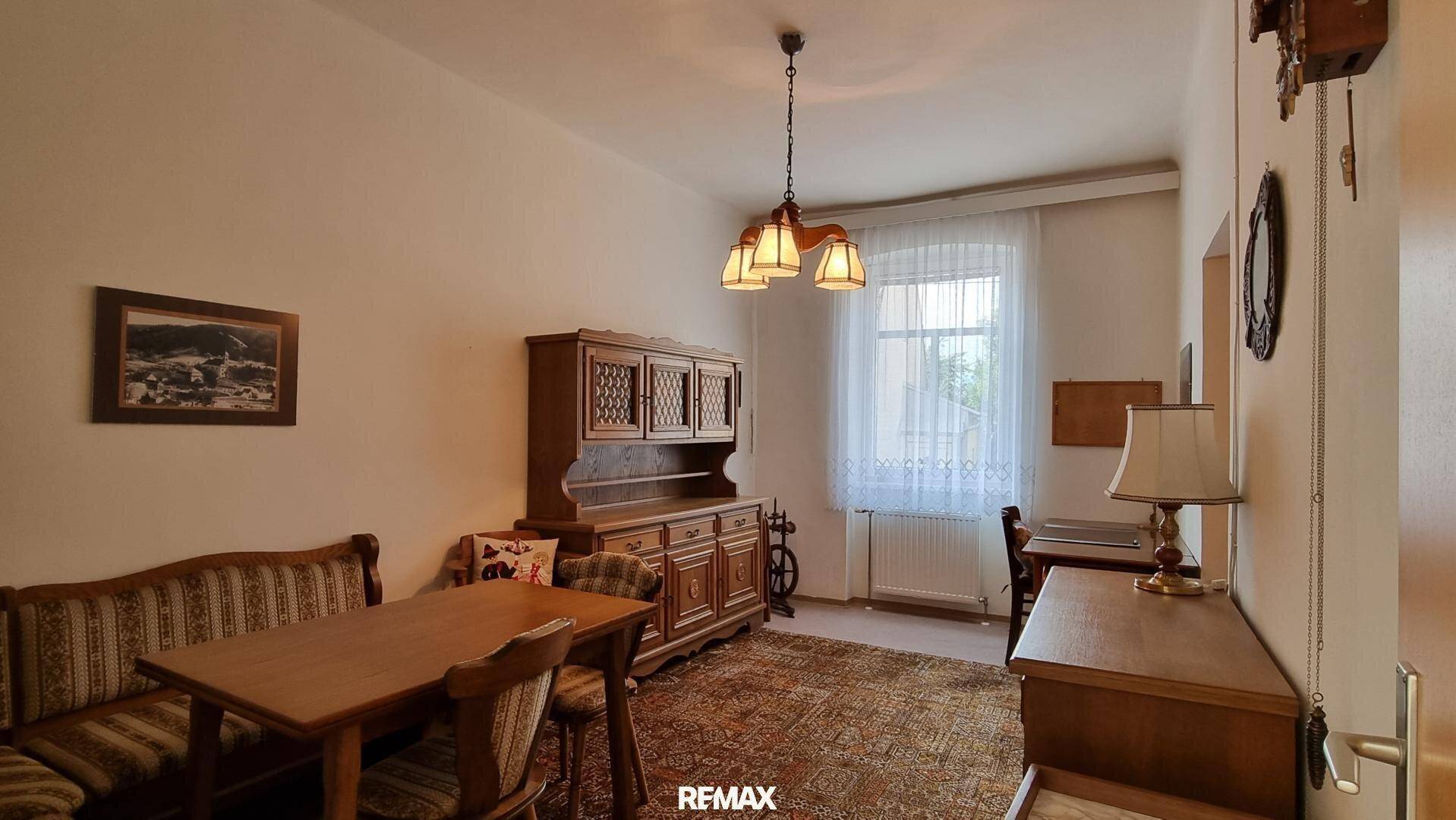 Traditionelles Esszimmer mit Holzmöbeln, Teppichboden und Fenster mit Vorhängen.