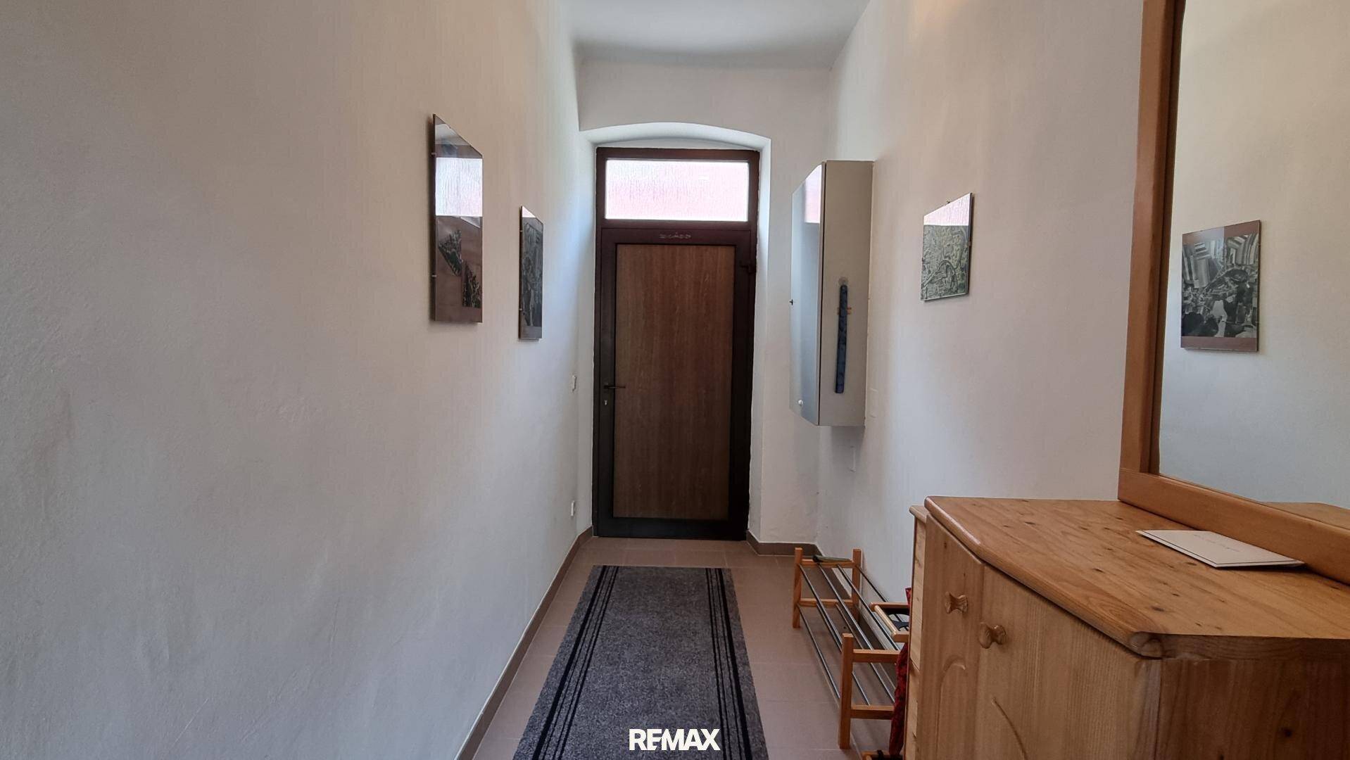 Heller Flur mit Holztür, Spiegel und Schuhregal, führt zum Eingangsbereich.
