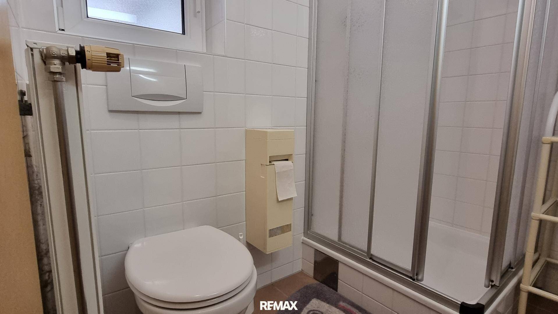 Badezimmer mit WC, Duschkabine und weißen Fliesen an Wänden und Boden.