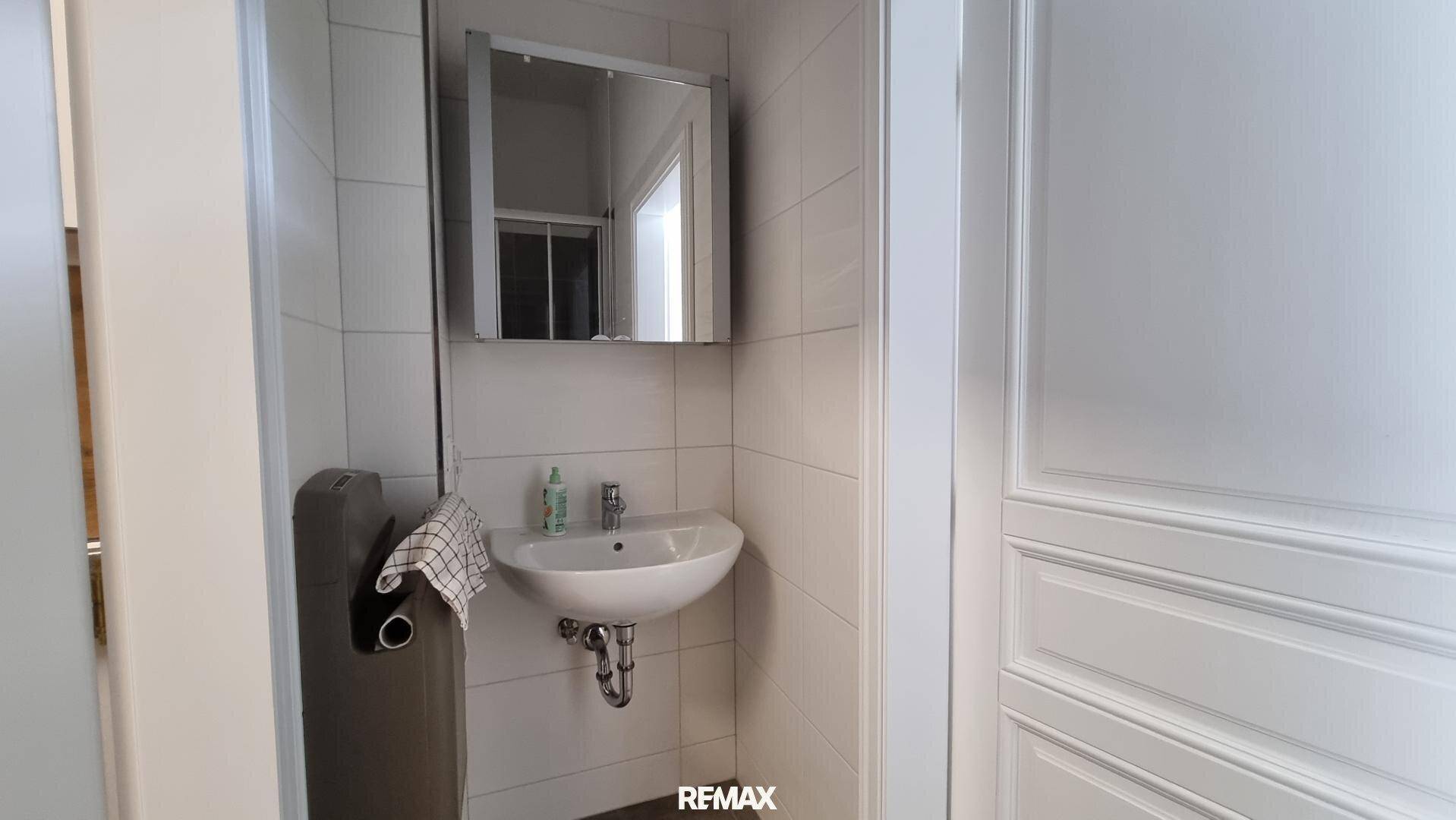 Kleines Gäste-WC mit Waschbecken, Spiegelschrank und weißen Fliesen an den Wänden.