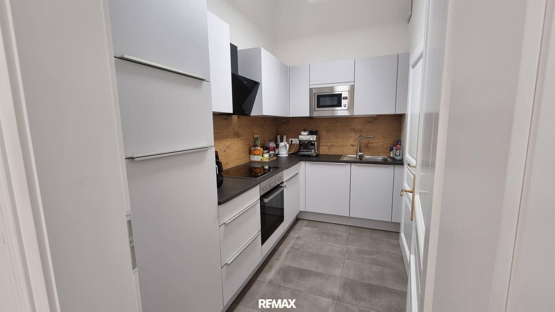 Moderne Küche mit weißen Schränken, dunkler Arbeitsplatte und Holzrückwand, ausgestattet mit Geräten.