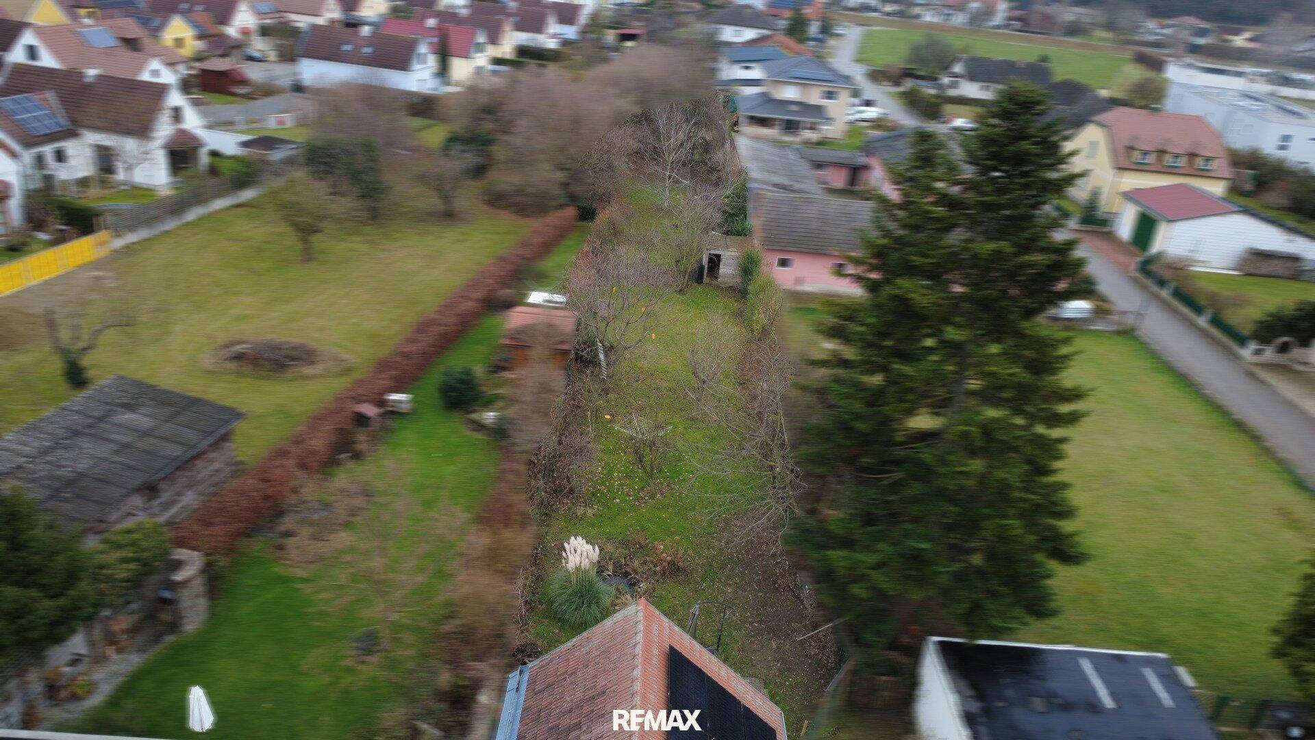 Luftaufnahme des langen Gartens mit Hecken und Bäumen, der viel Grünfläche bietet.
