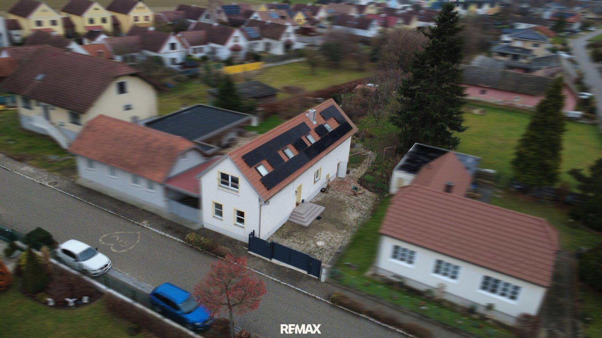 Luftaufnahme eines Einfamilienhauses mit Photovoltaikanlage auf dem Dach in einer Wohnsiedlung.