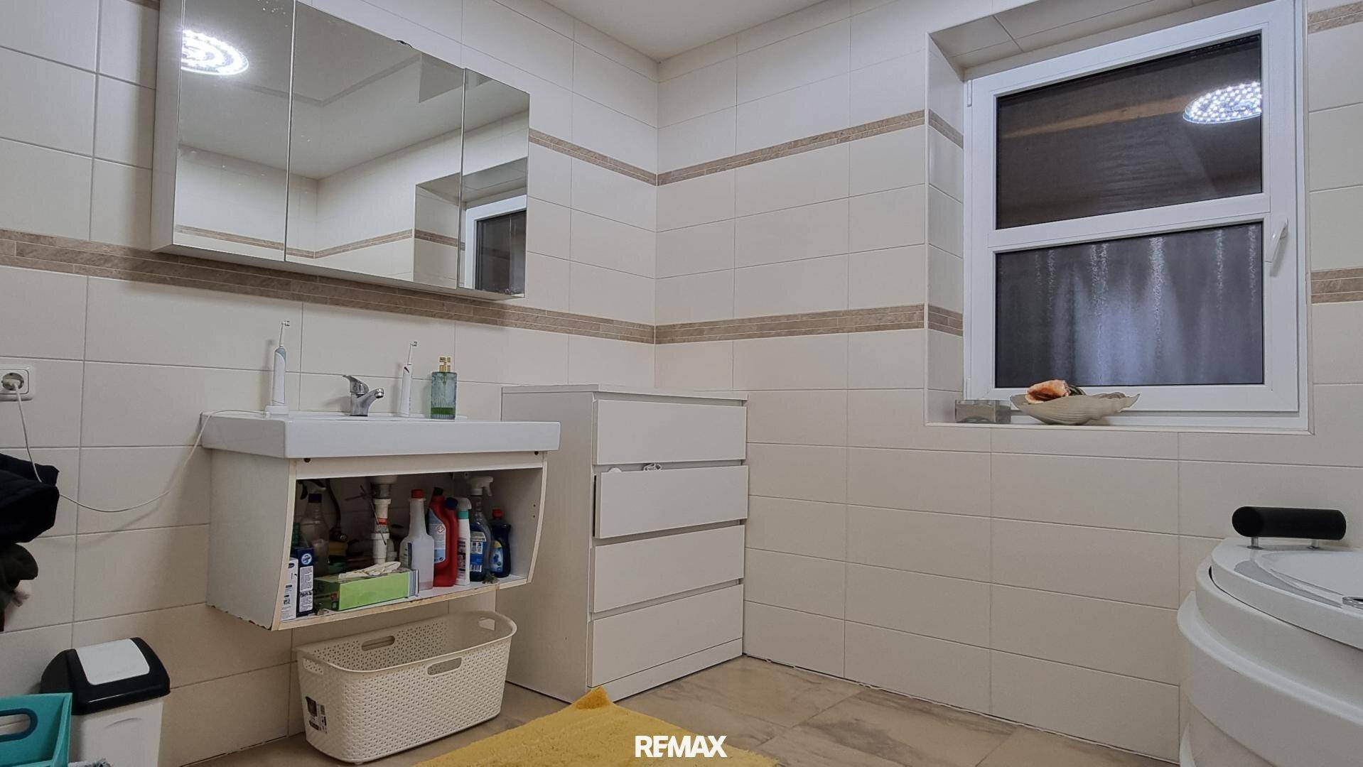 Badezimmer mit Waschbecken, Spiegelschrank, Kommode und einem Fenster für natürliche Belüftung.
