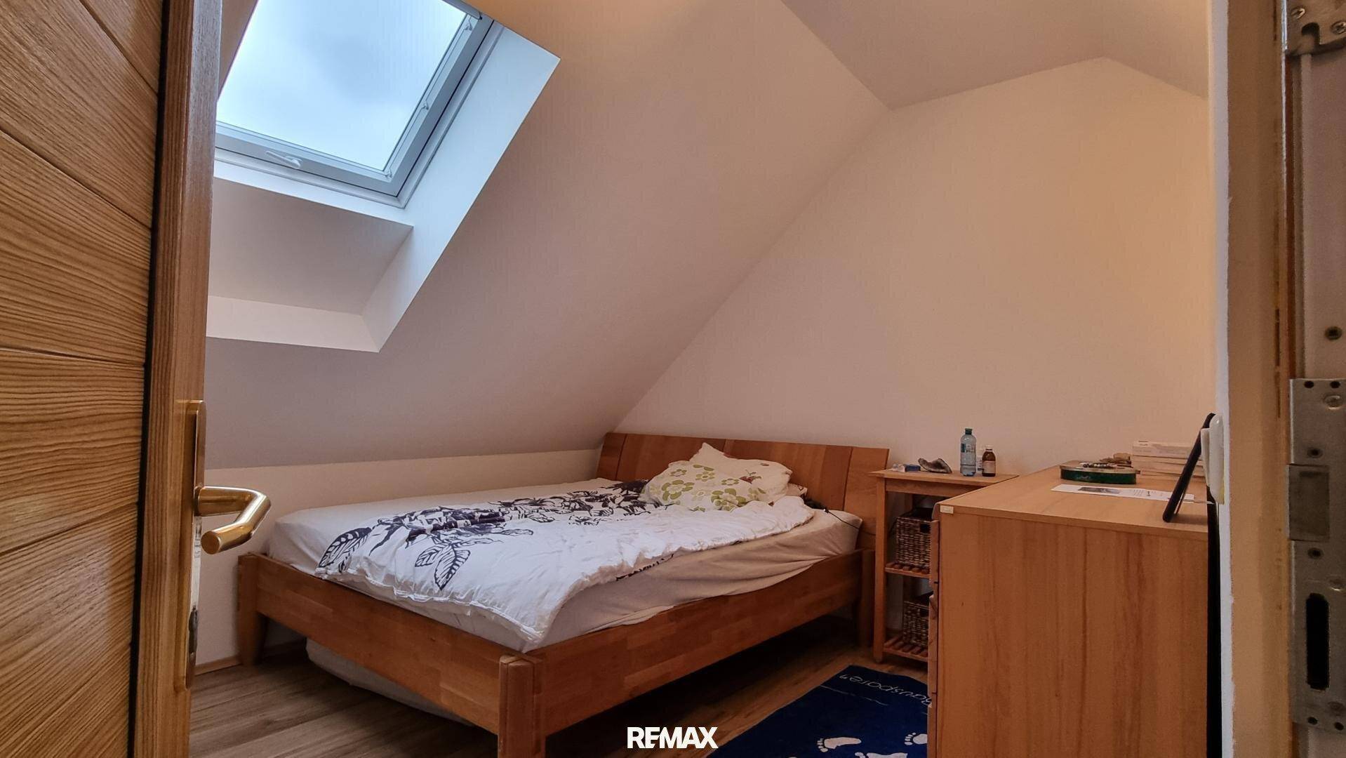 Helles Schlafzimmer im Dachgeschoss mit Holzbett, Nachttisch und einem Dachfenster für Tageslicht.