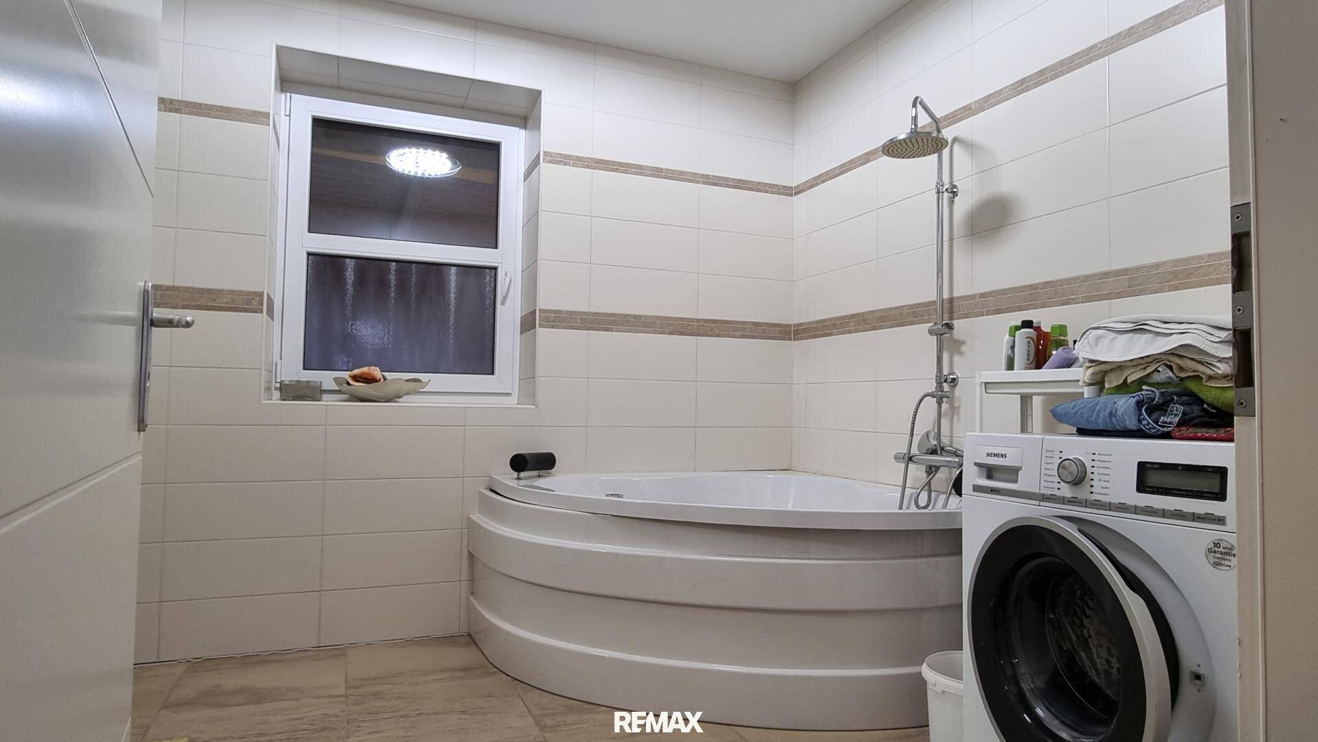 Badezimmer mit runder Badewanne, Duschvorrichtung, Waschmaschine und einem Fenster.