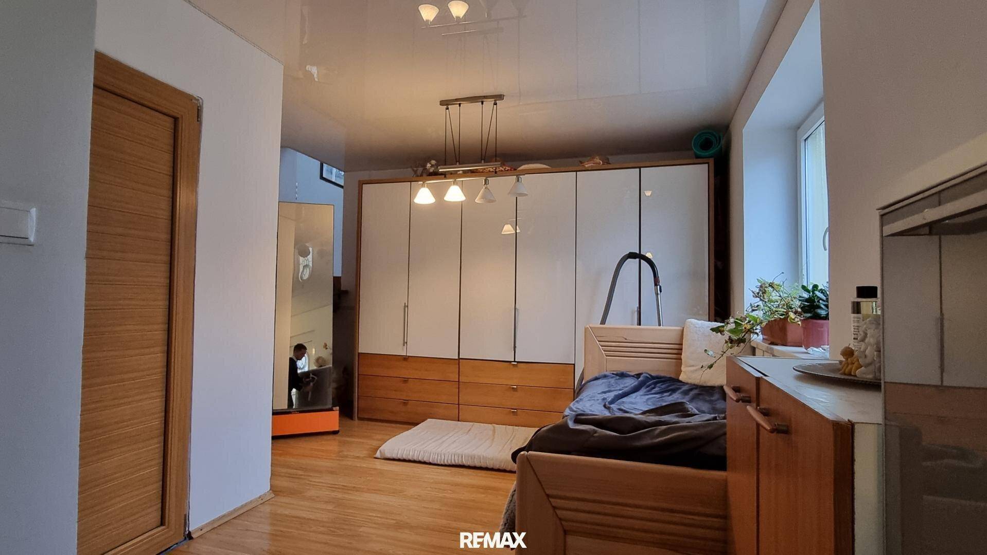 Schlafzimmer mit großem Kleiderschrank, Holzbett und Fenster, das viel Tageslicht hereinlässt.