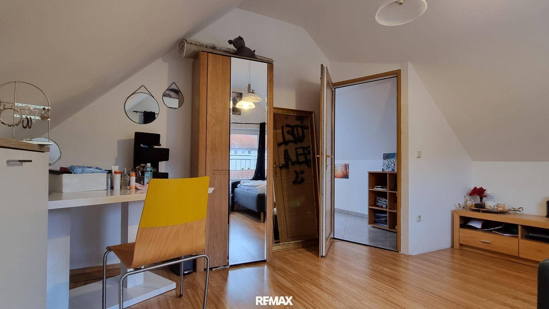 Helles Dachzimmer mit schrägen Wänden, Schreibtisch und Spiegelschrank, ideal als Arbeits- oder Gästezimmer.