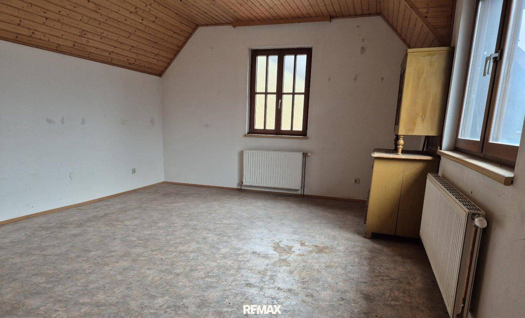 Dachbodenraum mit Fenster, Holzdecke und Heizkörper, bereit für Renovierung und Ausbau.