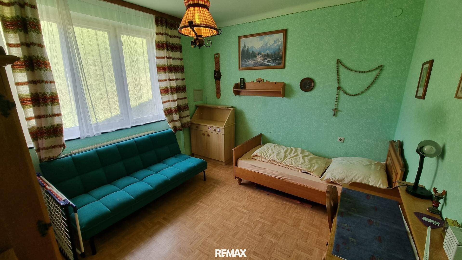 Schlafzimmer mit grün gestrichenen Wänden, Einzelbett und Sofa, hell und freundlich mit Fenster.