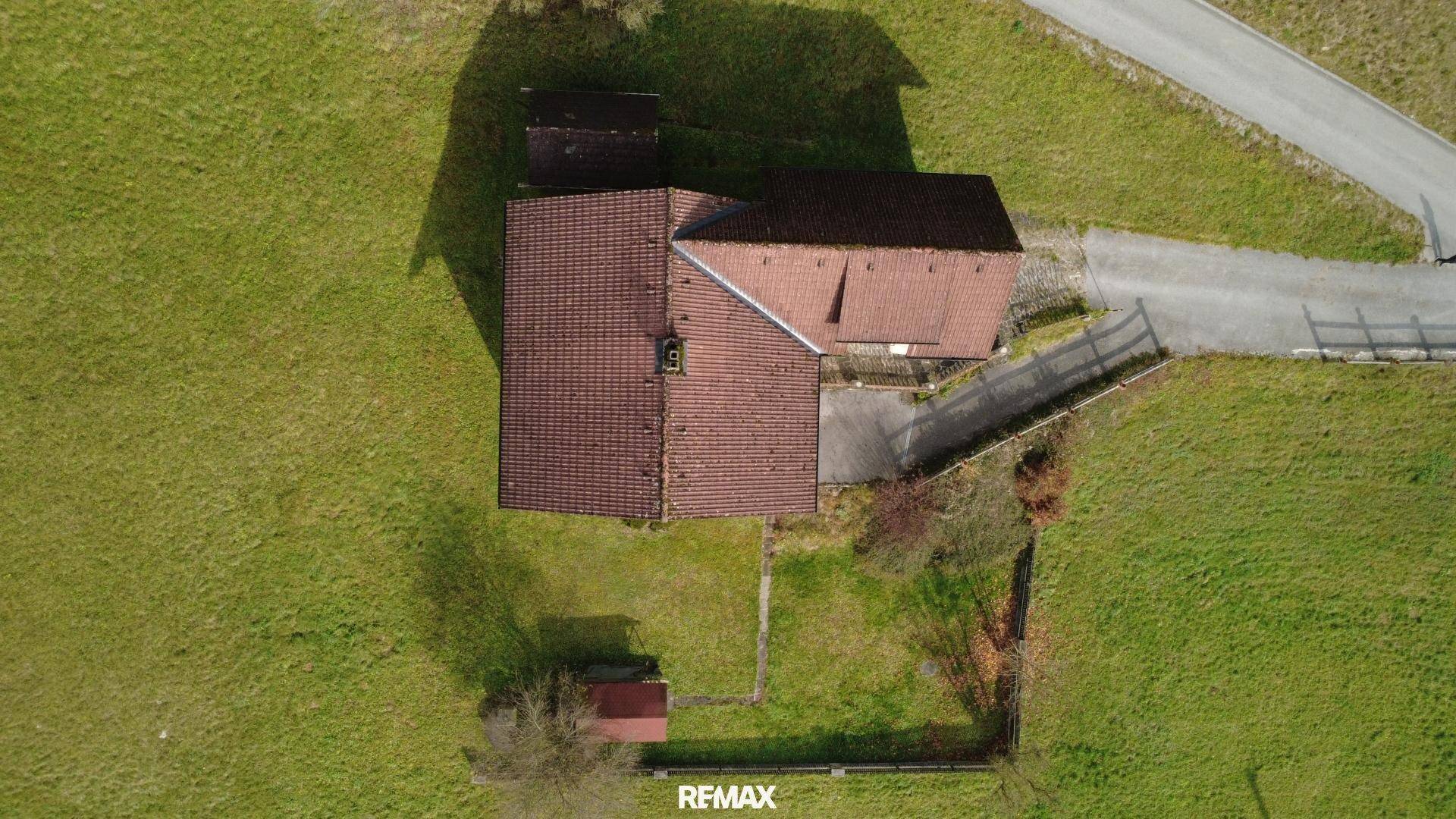 Luftaufnahme eines Anwesens mit einem Haus, einem Schuppen und weitläufigen grünen Feldern.