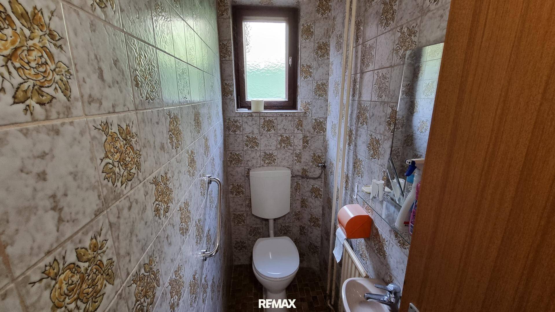 Separate Toilette mit gemusterten Fliesen, Fenster und kleinem Waschbecken, traditionell gestaltet.