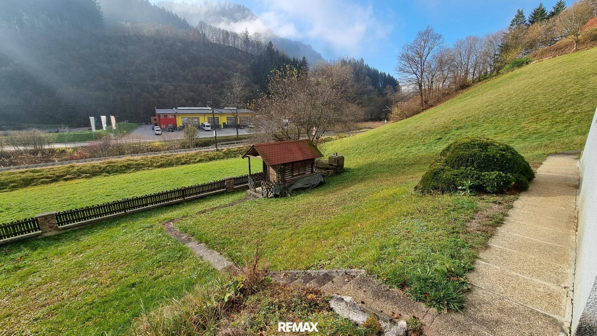 Grüner Gartenbereich mit kleinem Holzhaus und Blick auf die umliegende Landschaft.