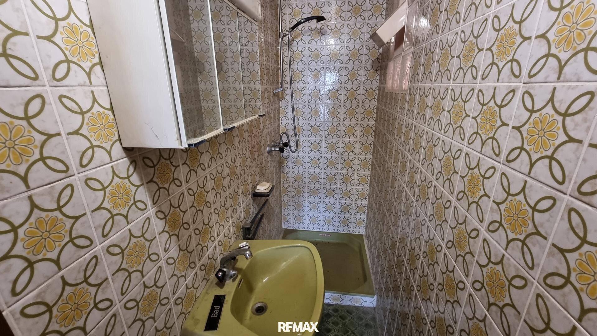 Kleines Badezimmer mit Duschbereich, gelben Fliesen und Waschbecken, funktional eingerichtet.