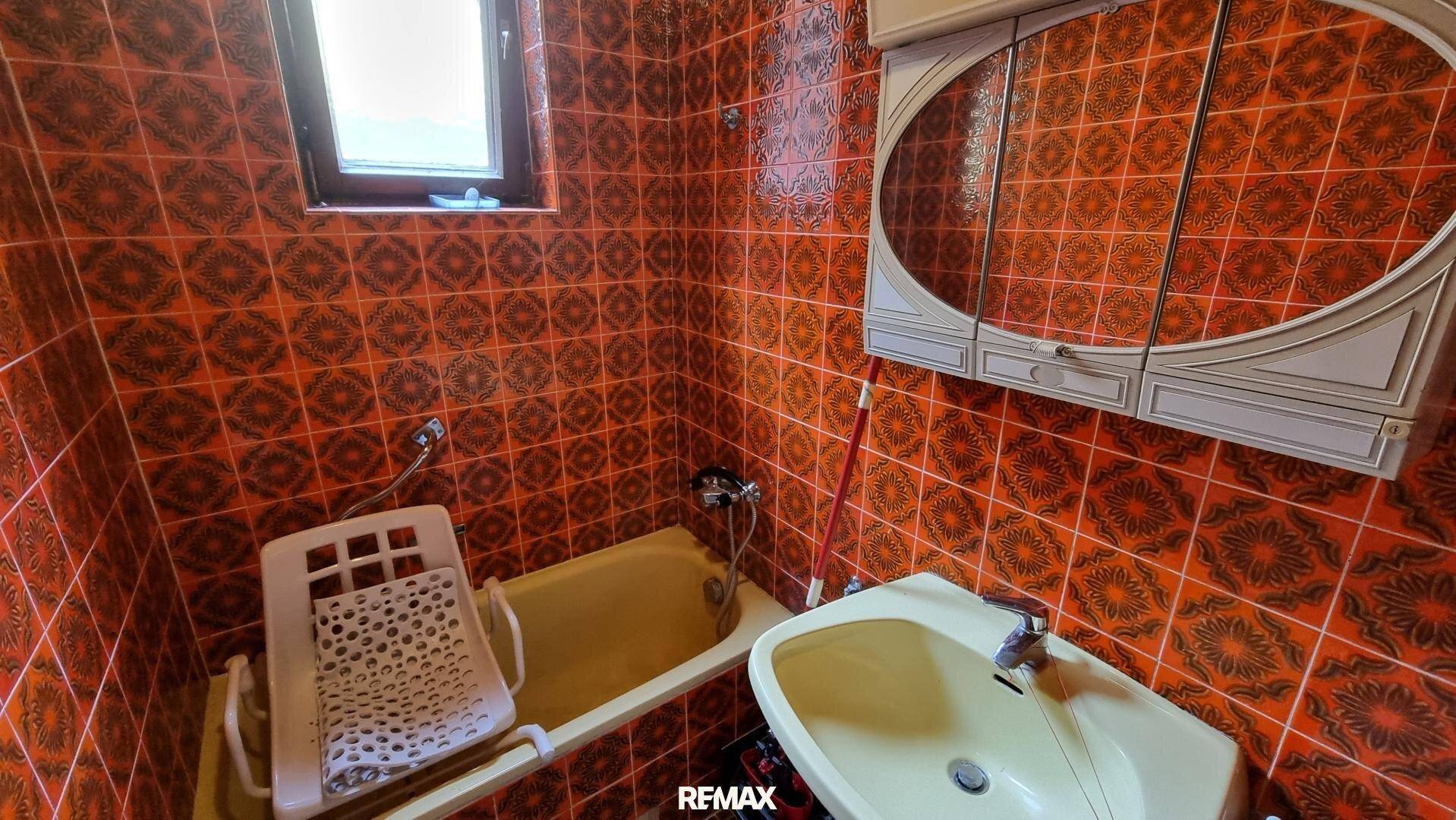 Badezimmer mit orangefarbenen Fliesen, Badewanne und Waschbecken im 80er-Jahre-Stil.