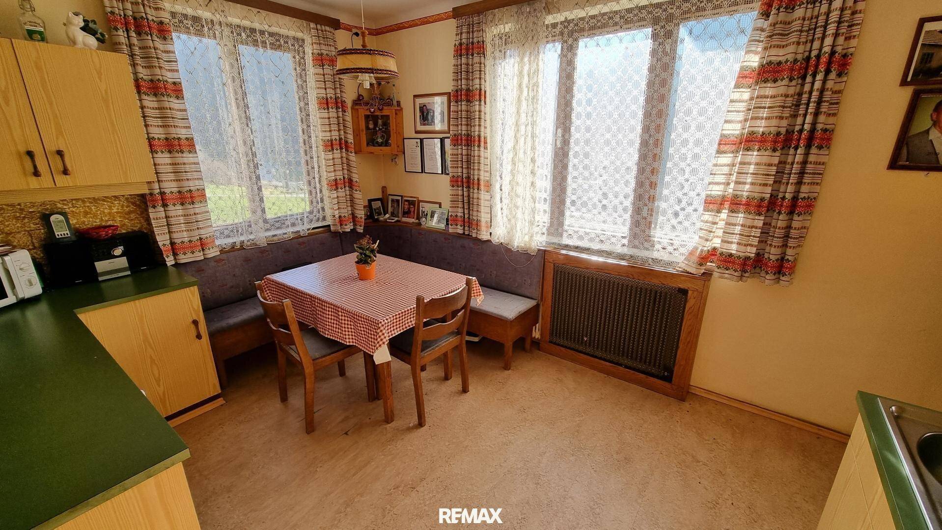 Essbereich in der Küche mit Eckbank, karierter Tischdecke und Blick ins Grüne durch große Fenster.