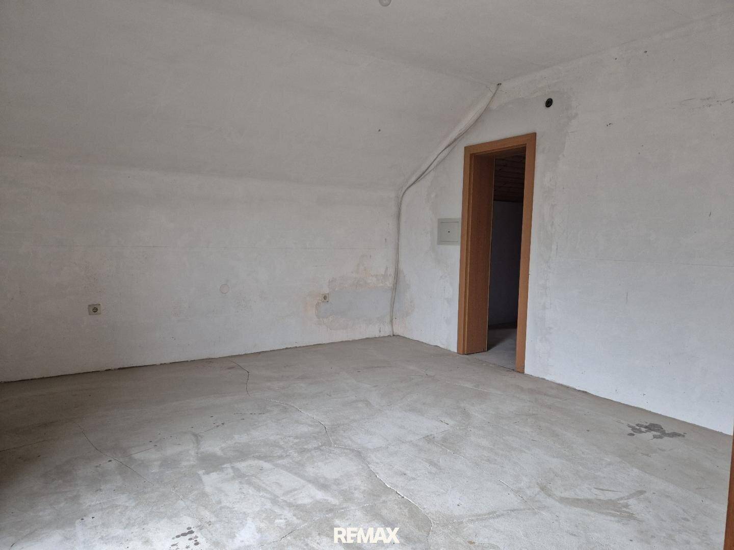 Unausgebauter Dachbodenraum mit rohen Wänden und Betonboden, bereit für zukünftigen Ausbau.