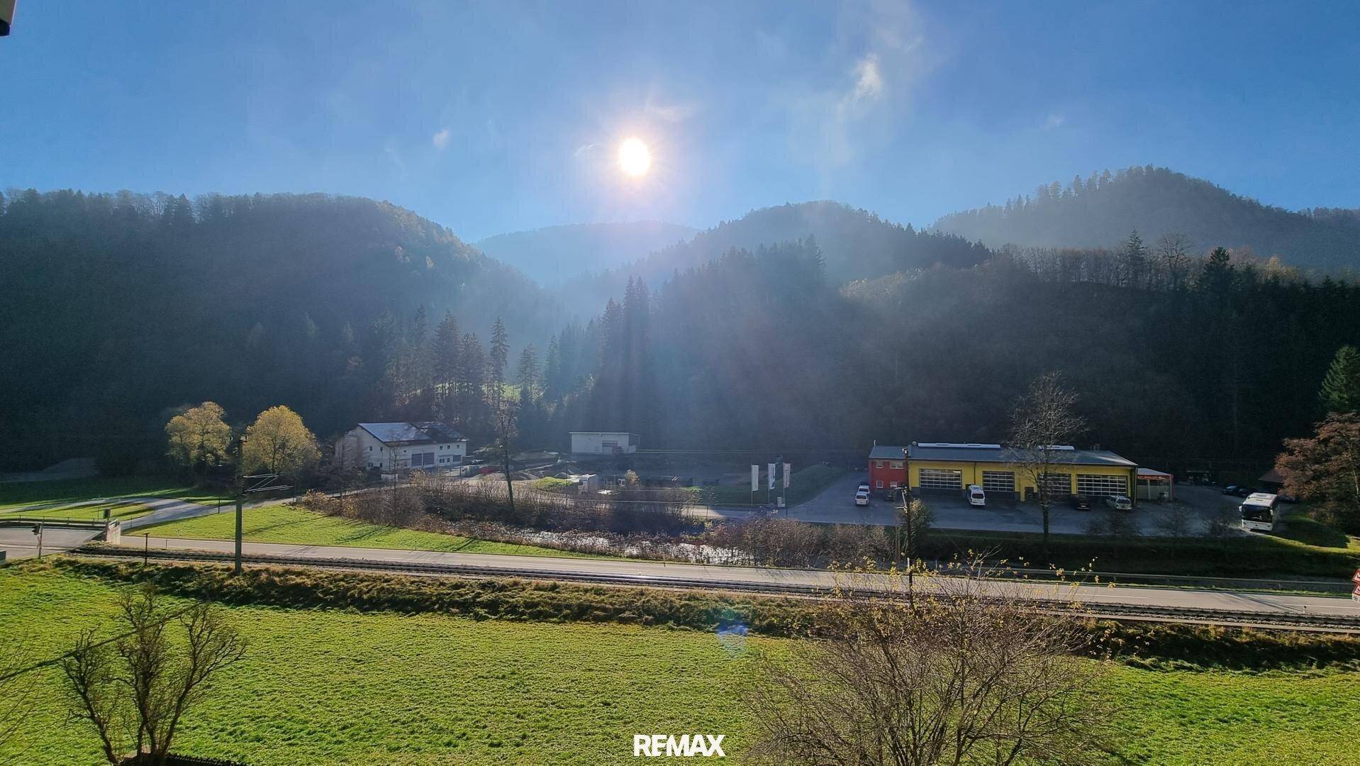 Weitläufiger Blick über die grüne Landschaft und die umliegenden Berge an einem sonnigen Tag.