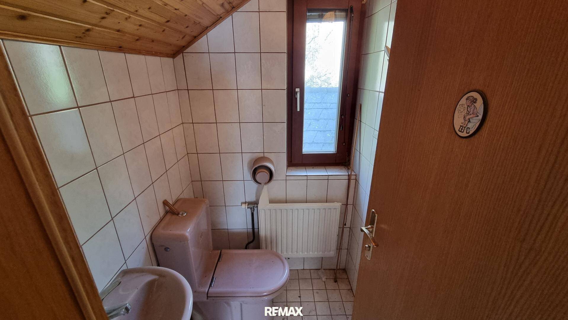 Separate Toilette mit rosa WC, Fenster und weißen Fliesen im Dachgeschoss, einfach gehalten.