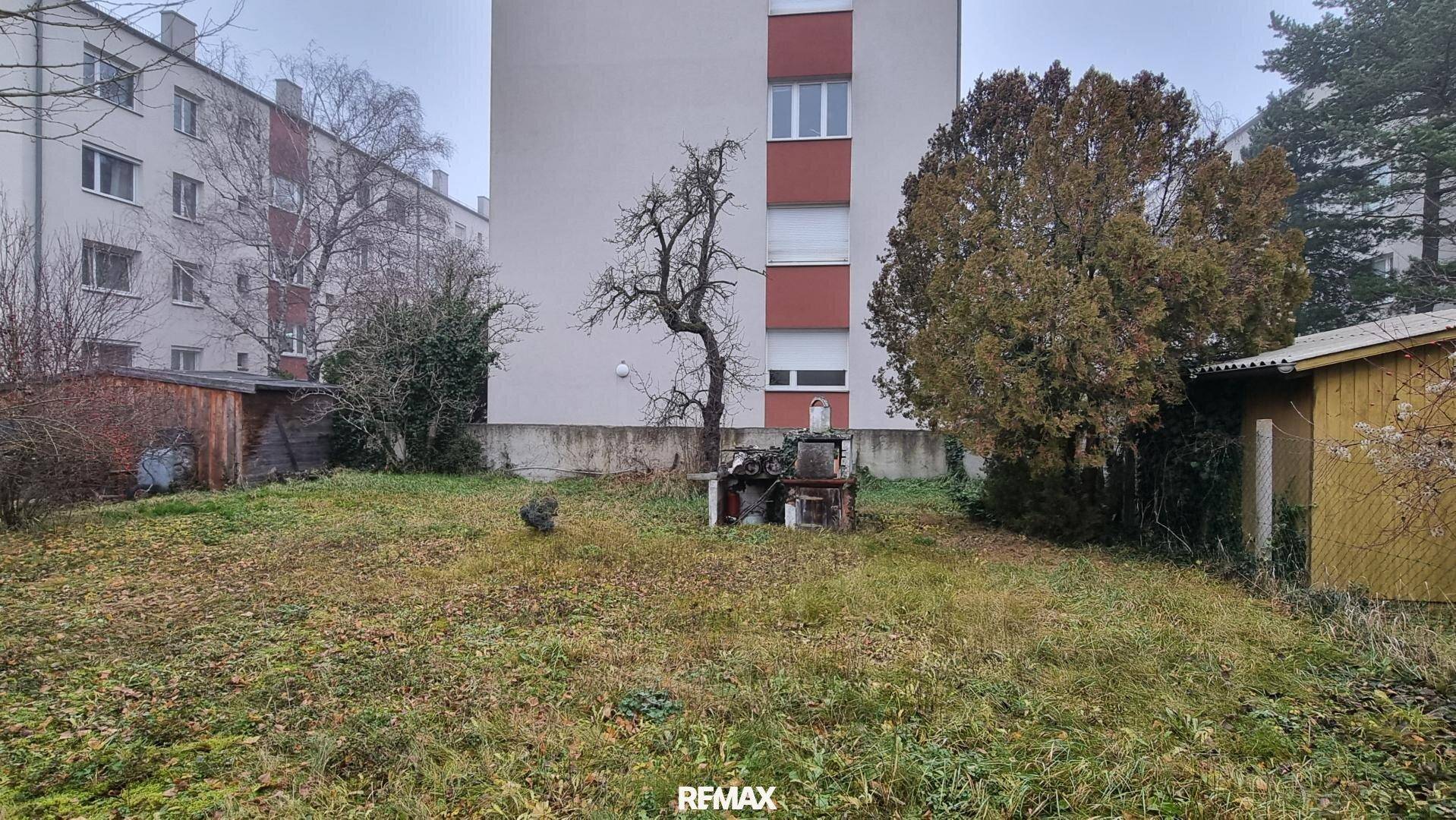 Großer Gartenbereich mit Rasen, Bäumen und einem kleinen Schuppen im Hintergrund, bietet viel Grünfläche.