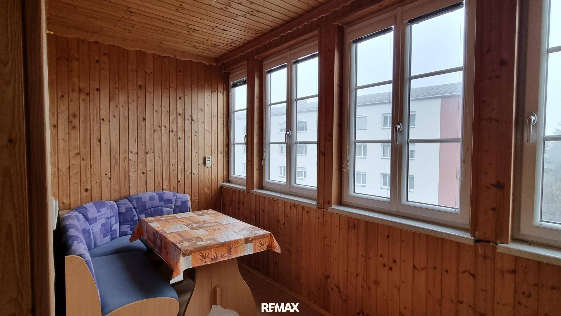 Gemütliche verglaste Loggia mit Holzverkleidung, Sitzbank und Tisch, ideal für entspannte Stunden.