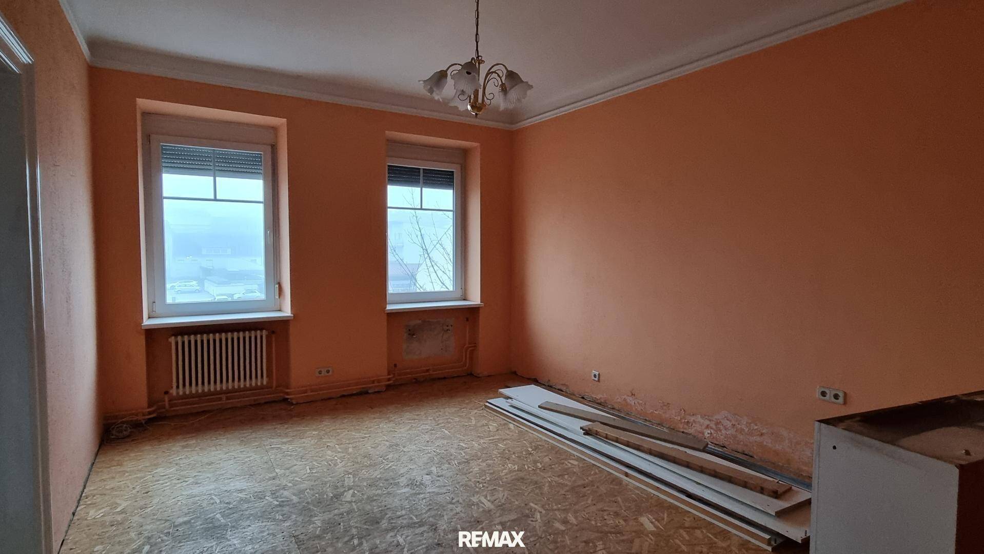 Geräumiges Zimmer mit orangefarbenen Wänden, zwei Fenstern und Heizkörpern, bietet viel Platz.