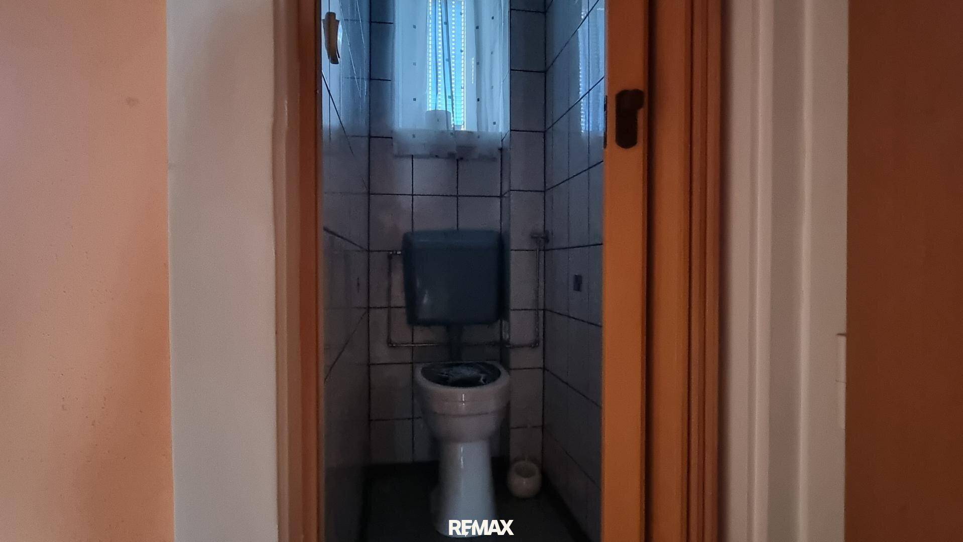 Kleines WC mit Fliesen an den Wänden und einem Fenster für Belüftung, funktional und einfach.