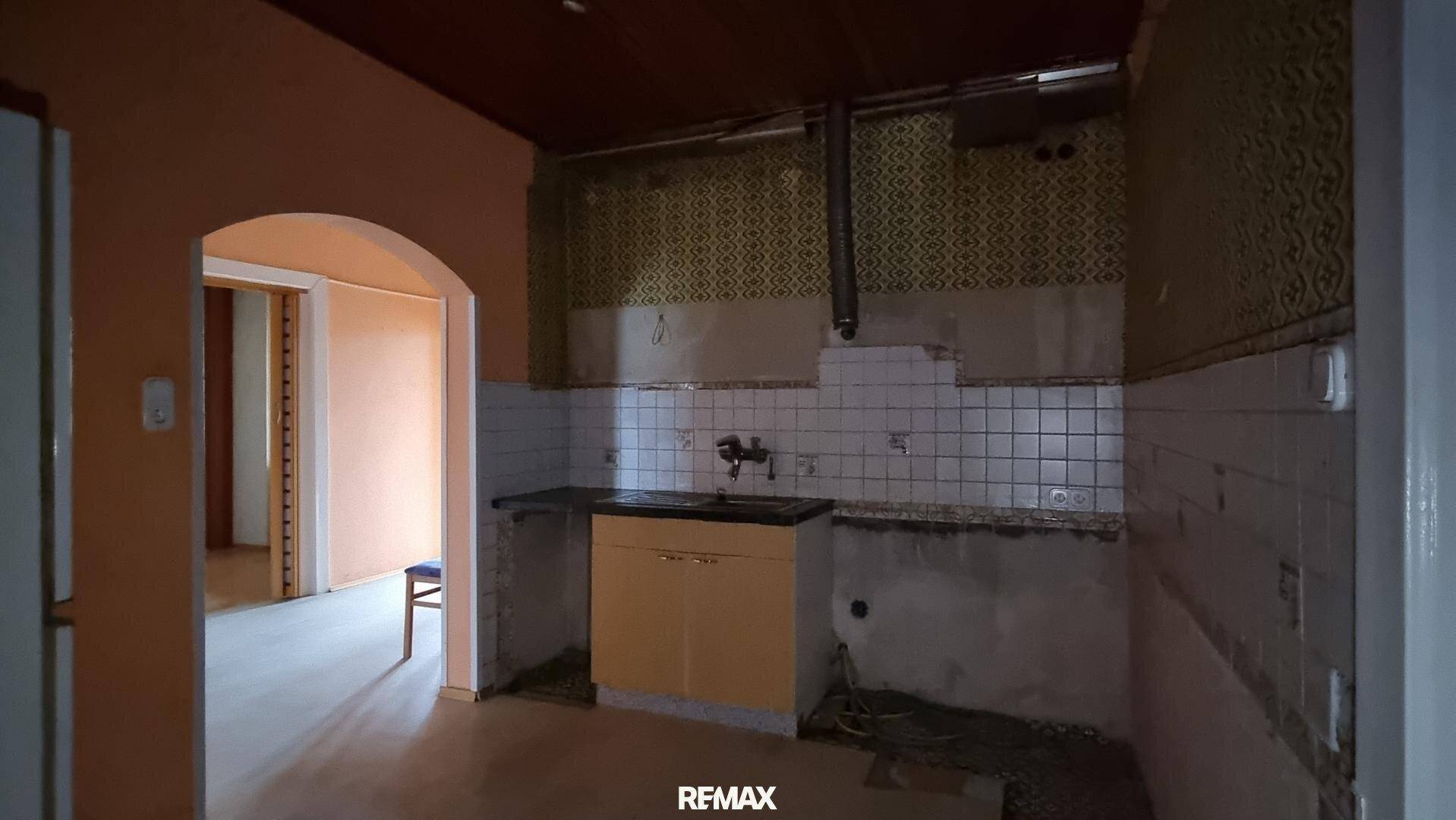Küche in Renovierung mit alten Fliesen, Spüle und sichtbaren Installationen, bereit für eine Neugestaltung.