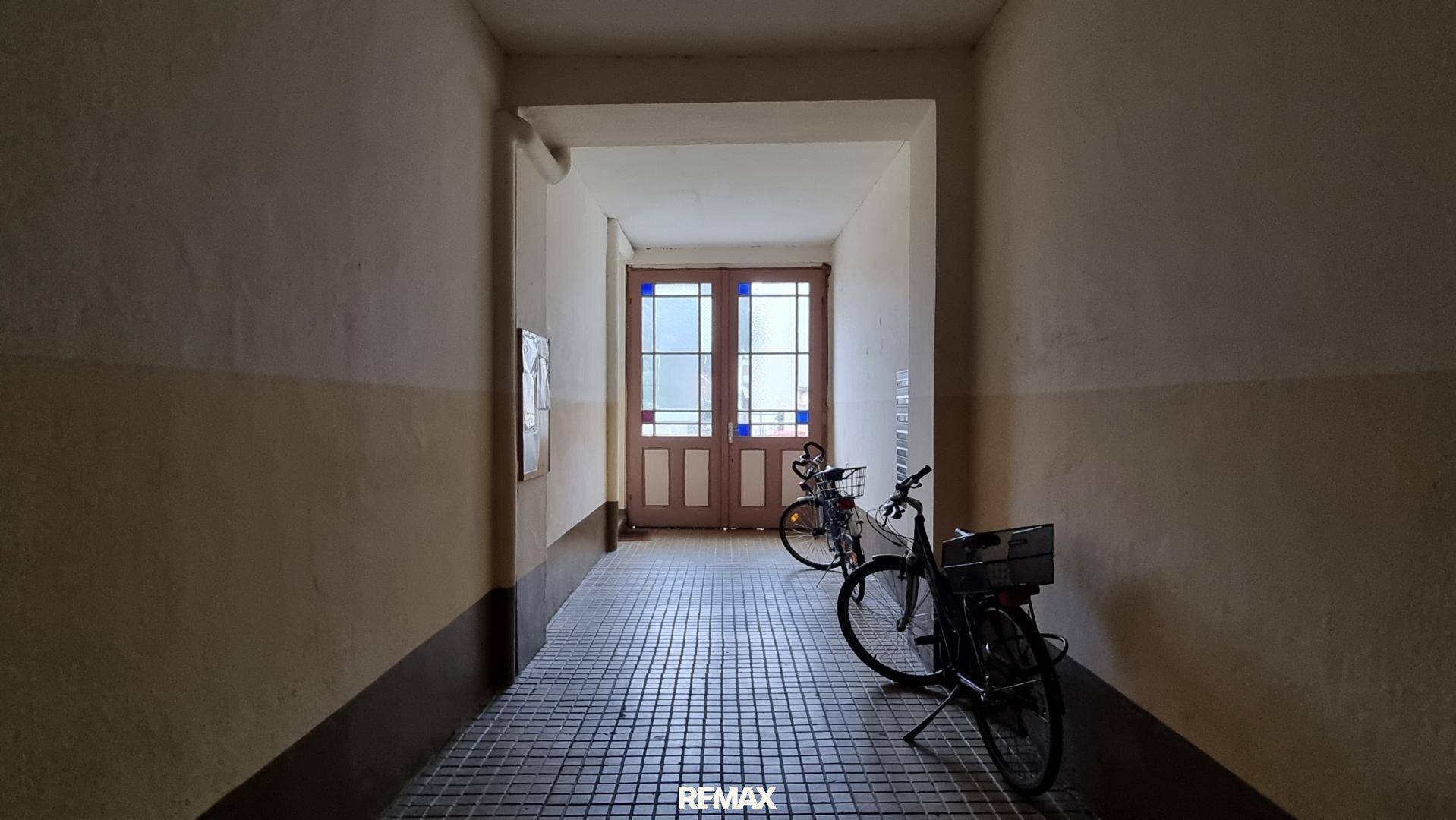 Eingangsbereich mit Fliesenboden, Fahrrädern und einer verglasten Doppeltür, die Tageslicht hereinlässt.